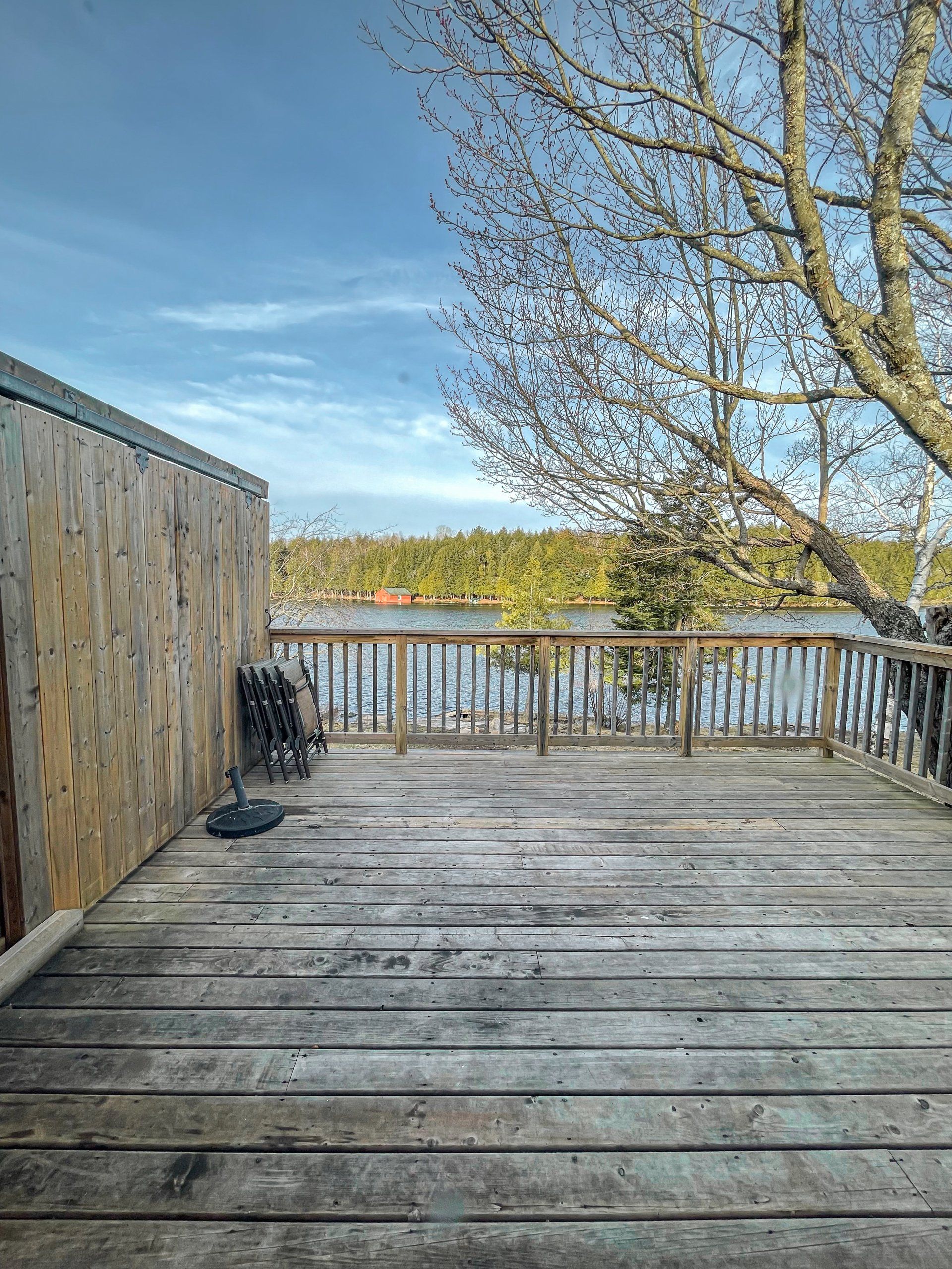 Wooden deck overlooking a lake with a fence, bare tree branches, and a blue sky
