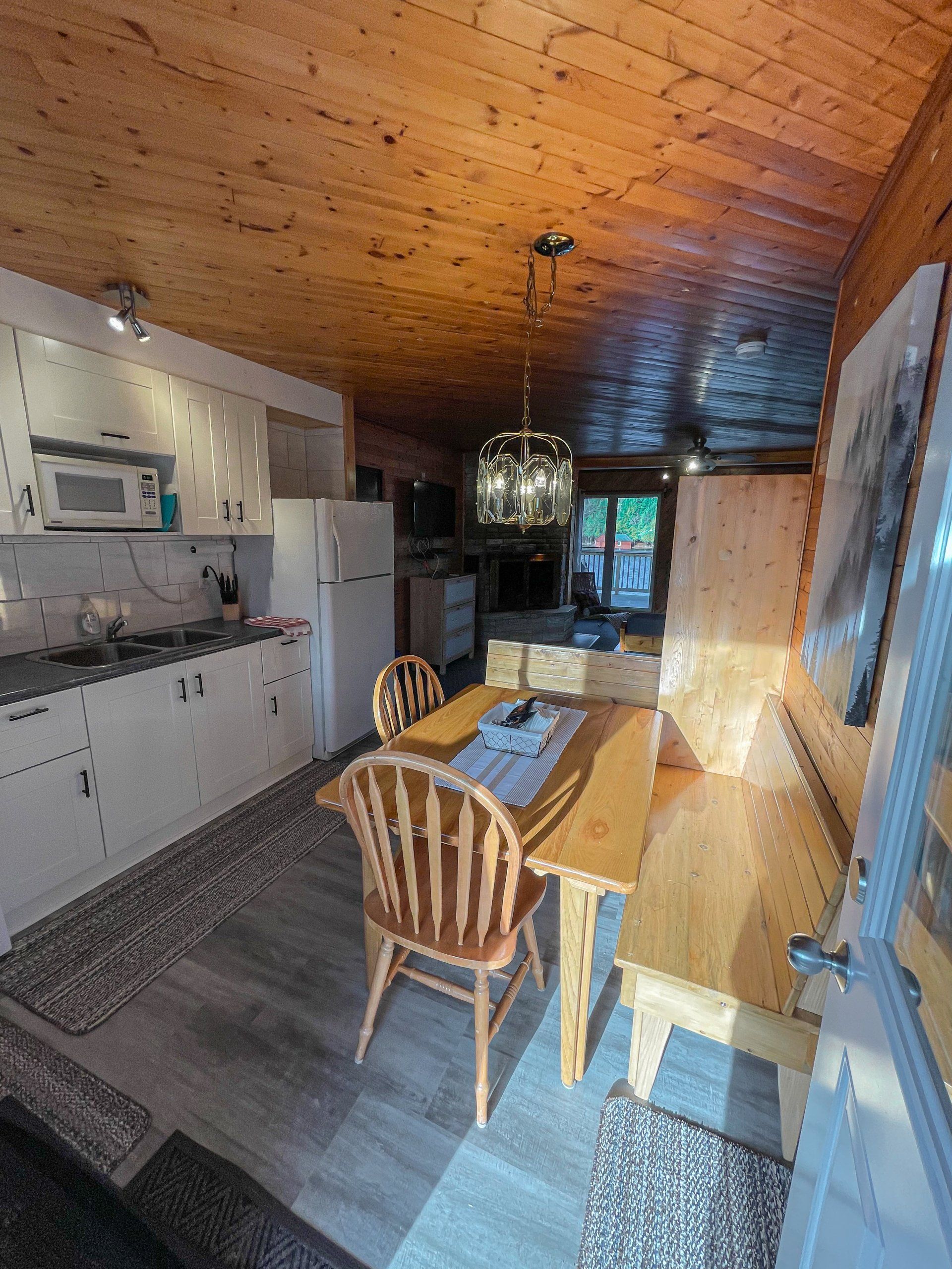 Long narrow kitchen-dining room with wood ceiling, white cabinets, long table, and large windowed doors.