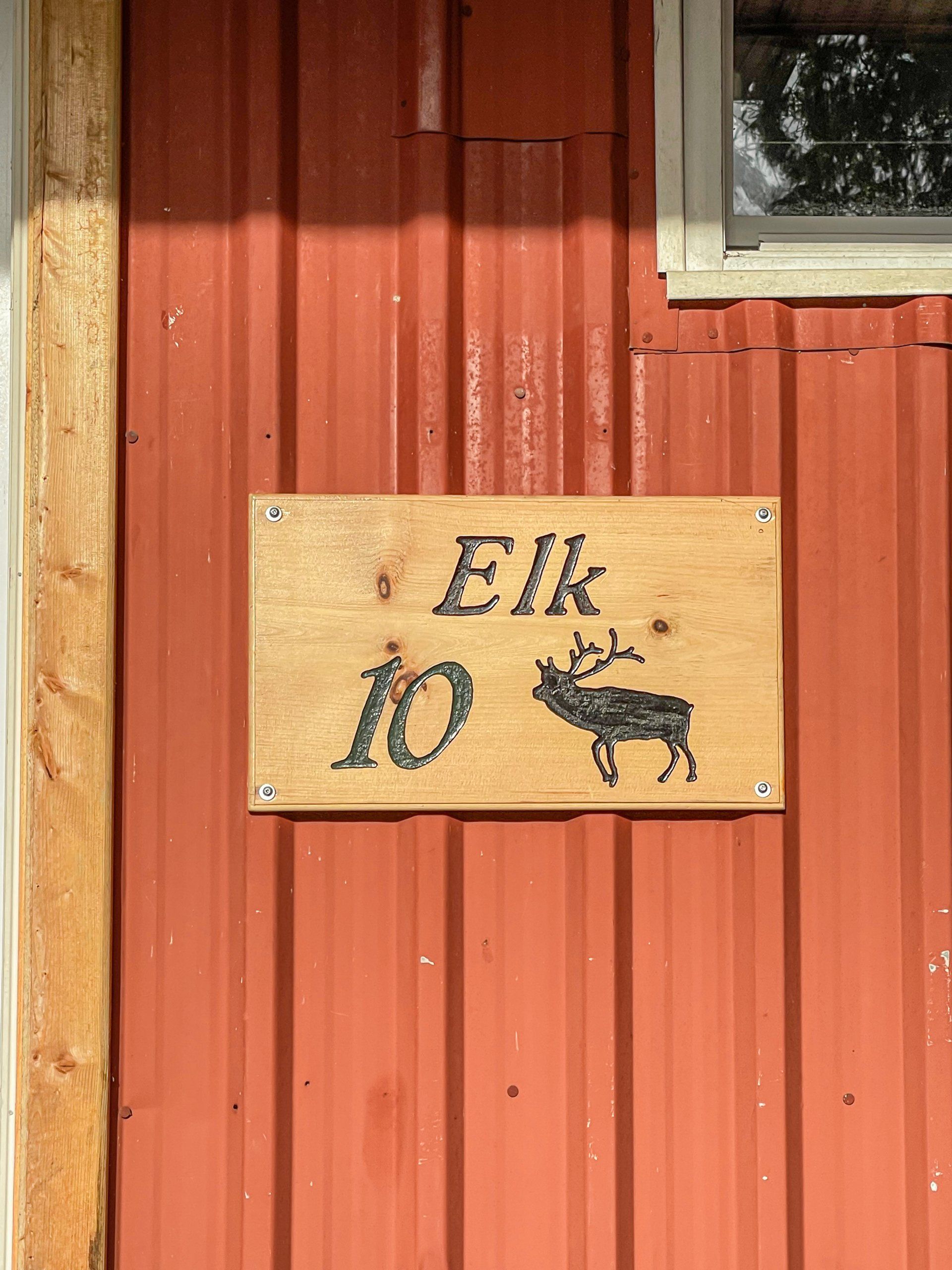 Wooden sign reading “Elk 10” with a black elk silhouette on a red wooden wall.