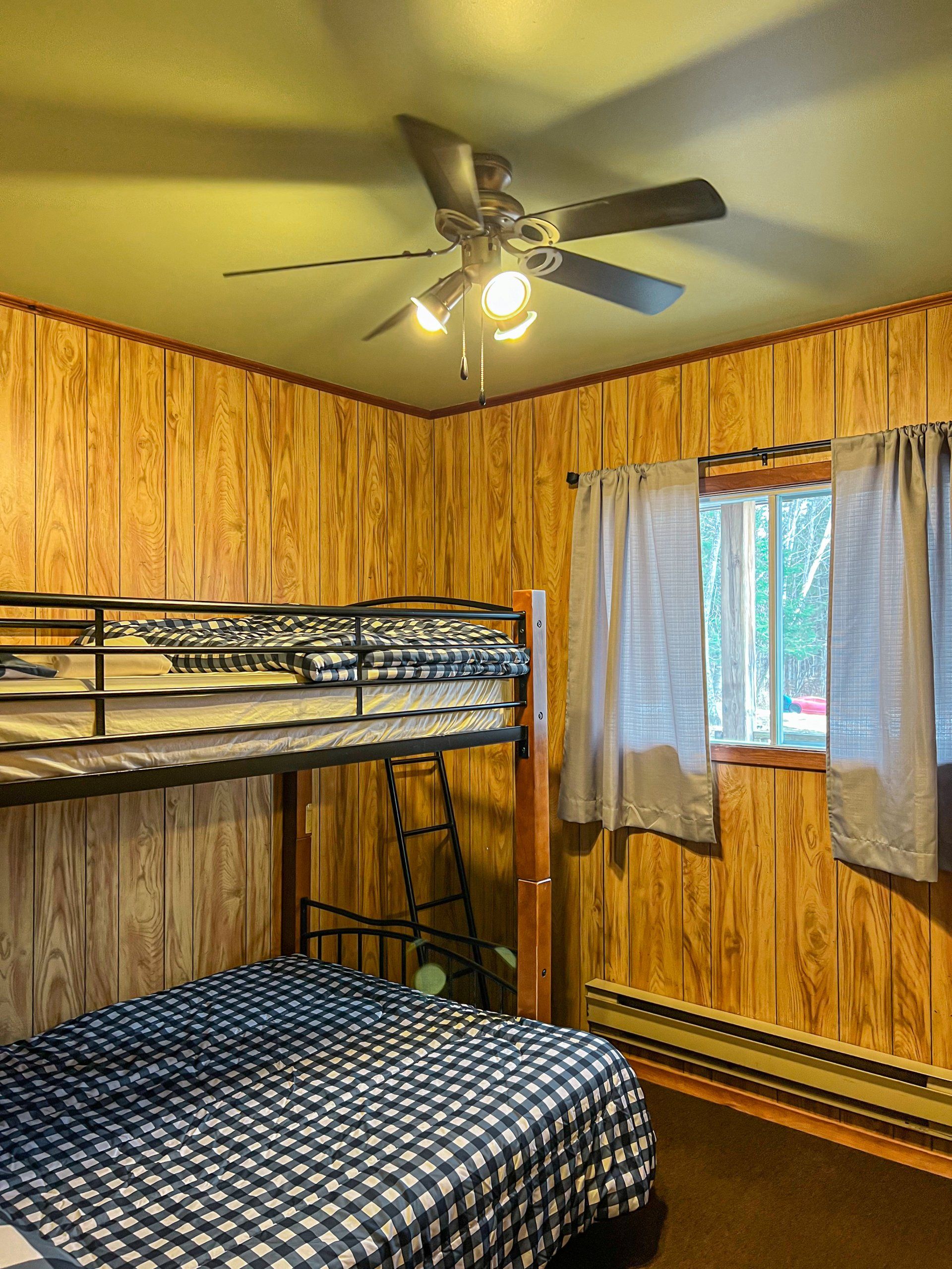 Wood-paneled bedroom with bunk beds, a ceiling fan, and a window with curtains