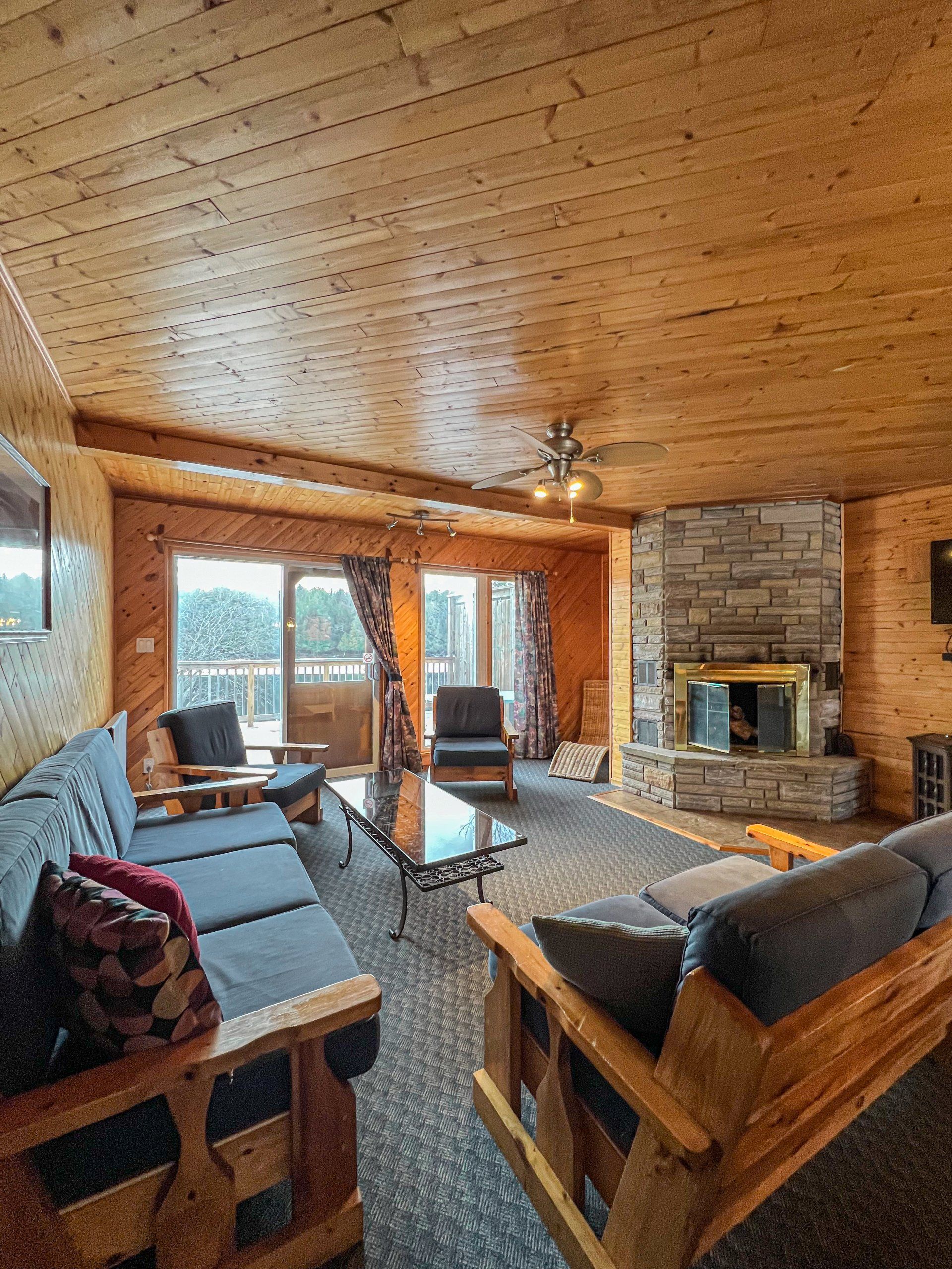 Cozy log cabin living room with wood beams, stone fireplace, large windows, and rustic furniture.