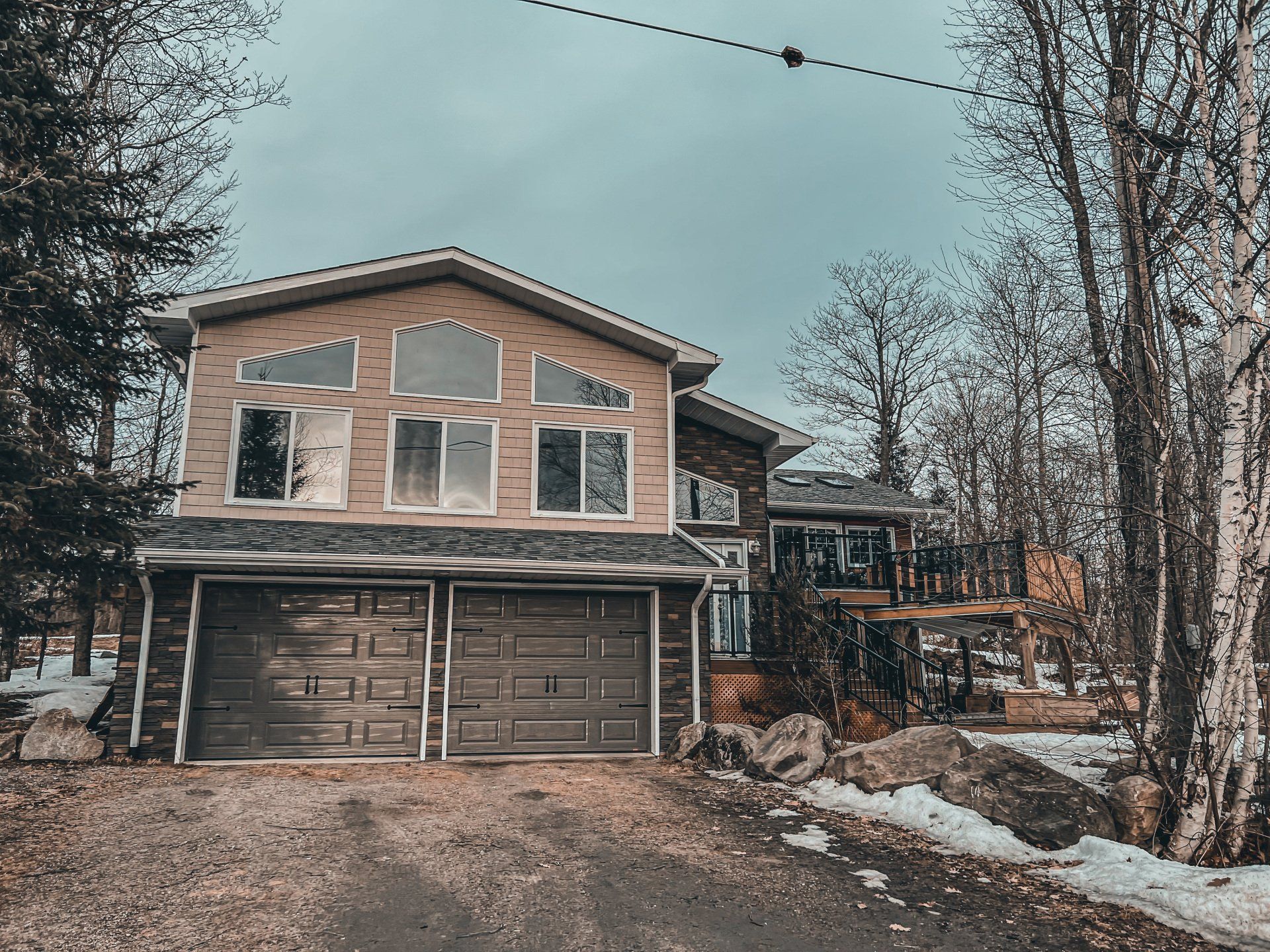 Two-story house with a double garage and snowy driveway in a wooded neighborhood