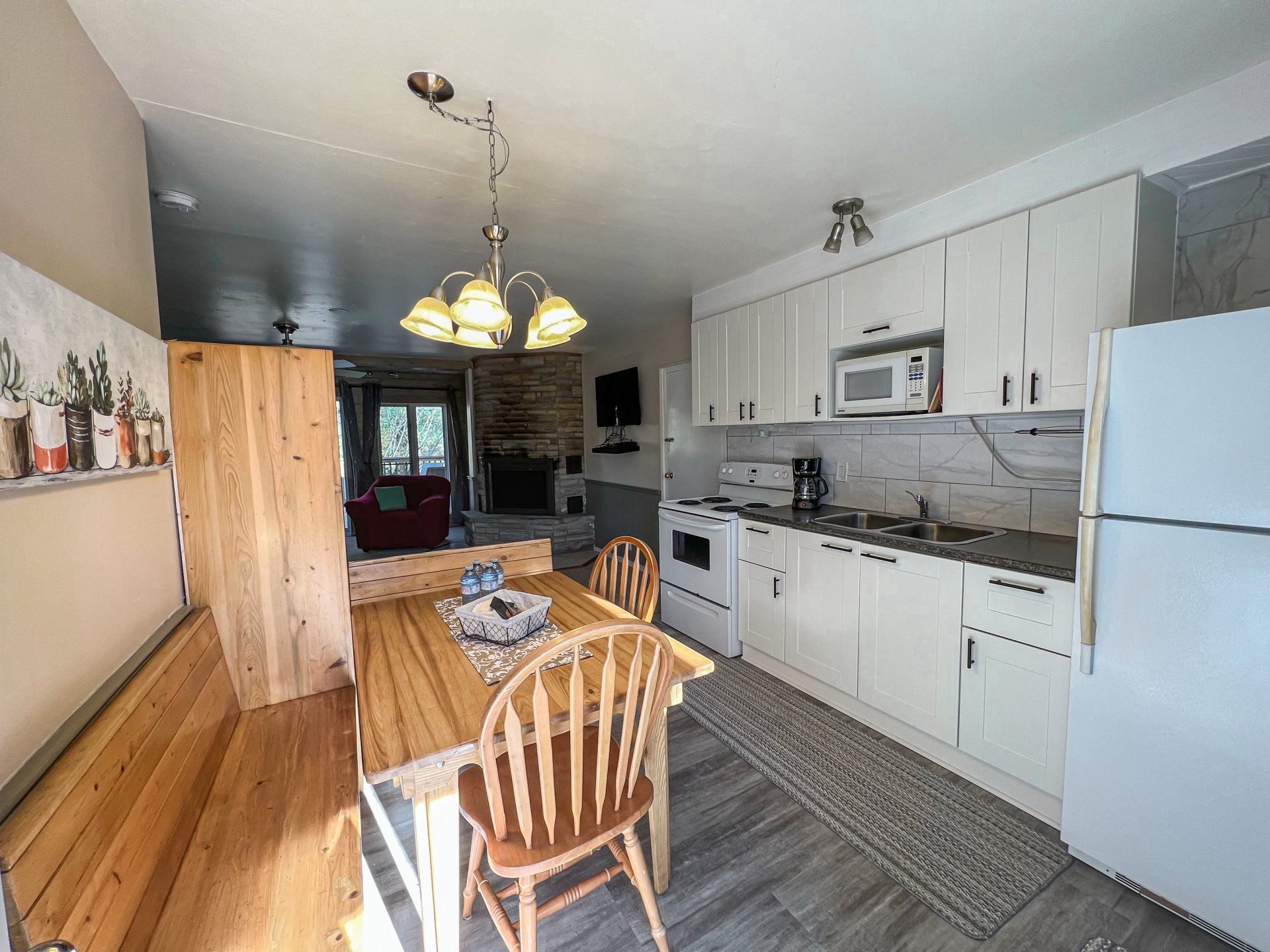 Bright kitchen with white cabinets, wooden table and chairs, refrigerator, and hanging light fixture