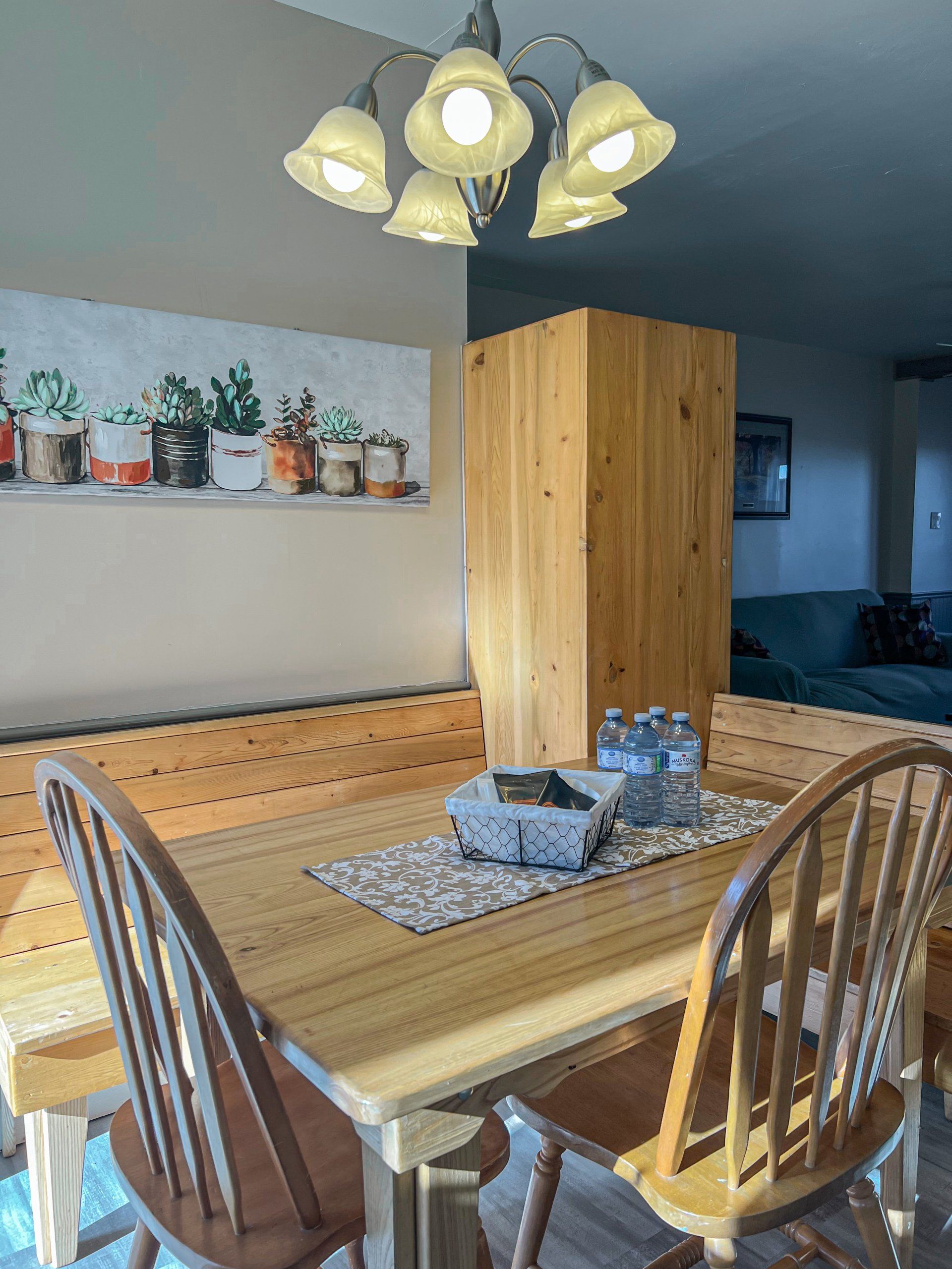 Dining room with wooden table and chairs, pendant light, and a view into a cozy living area.
