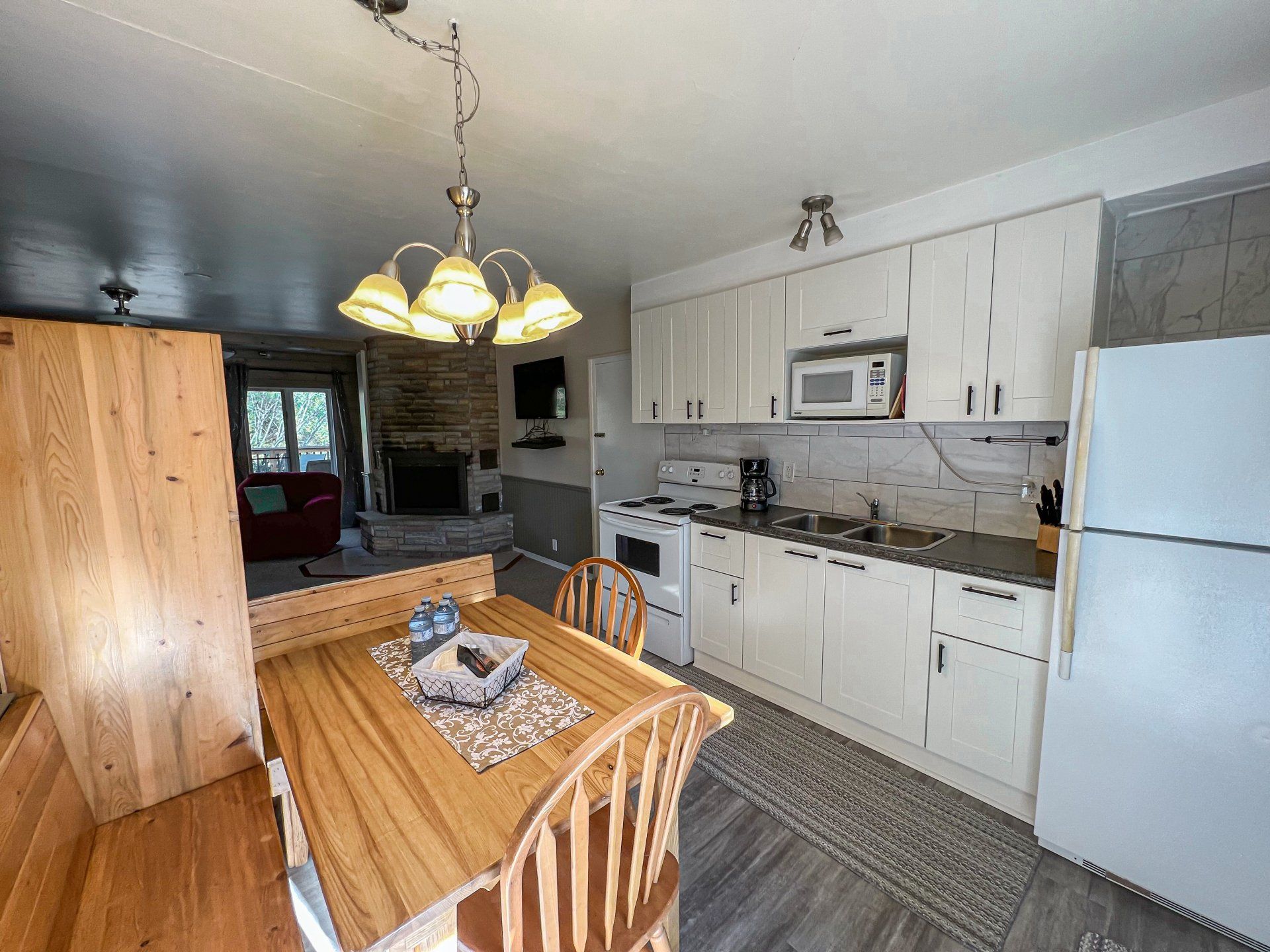 Small kitchen and dining area with white cabinets, wooden table, chandelier, and refrigerator.