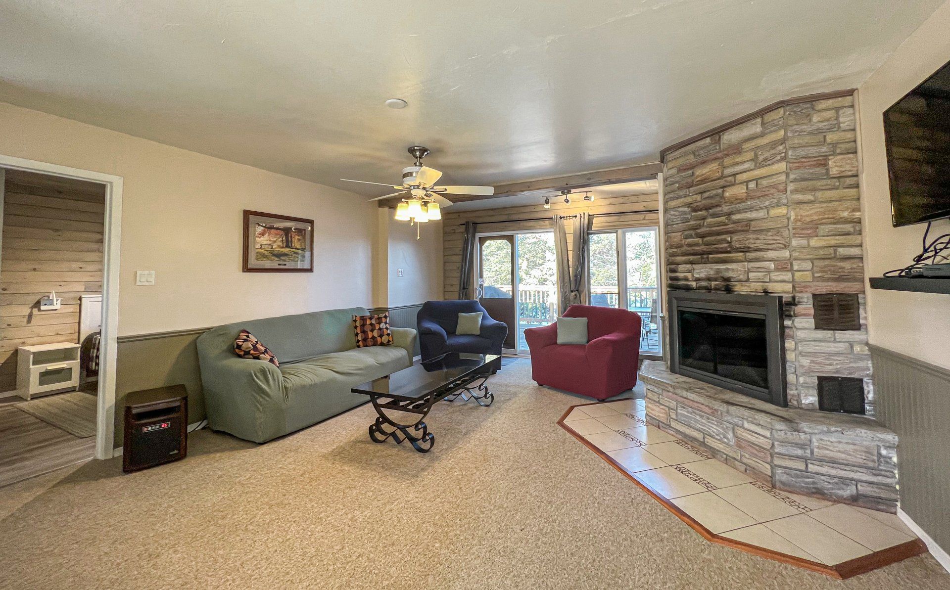 Living room with green sofa, red chair, stone fireplace, ceiling fan, and sliding glass doors