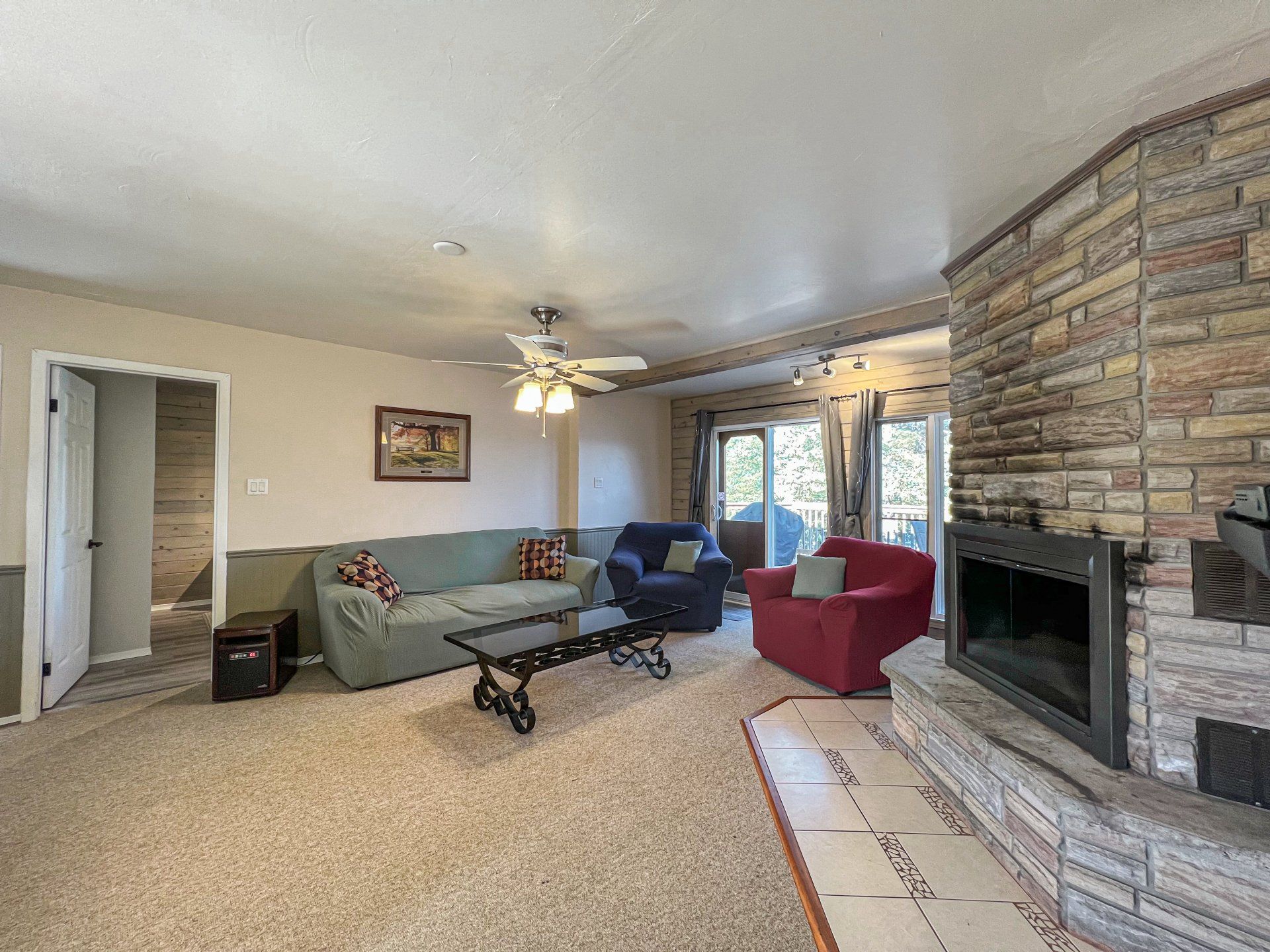 Living room with stone fireplace, green sofa, red chair, blue recliner, and ceiling fan