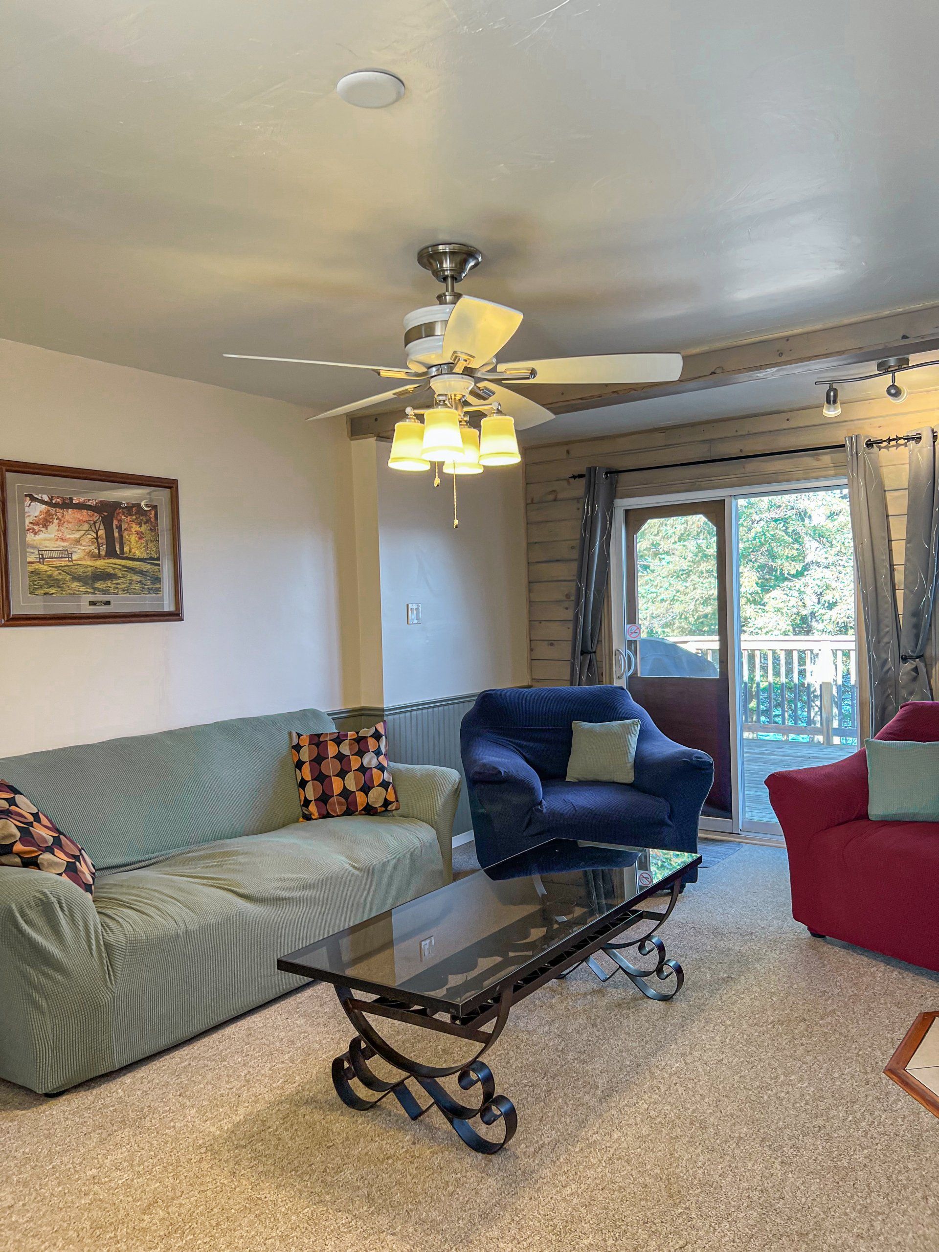 Living room with sofas, glass coffee table, ceiling fan, and sliding doors to a deck
