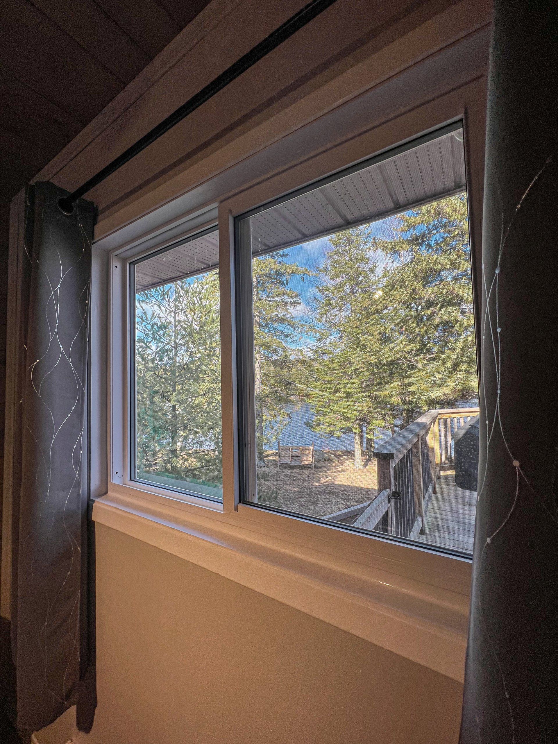 View through a window with trees and blue sky outside, framed by dark curtains.