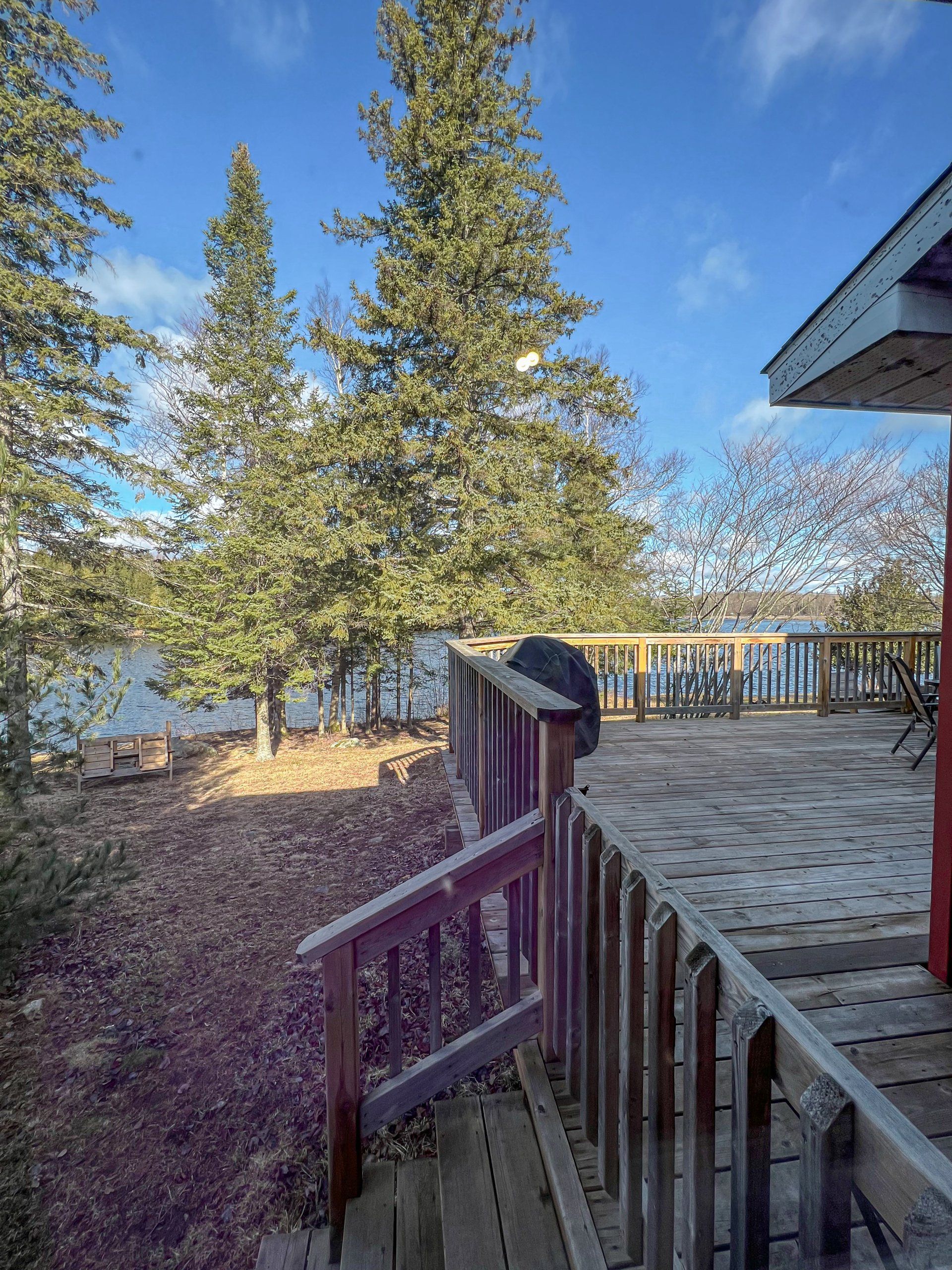 Snowy deck and steps overlooking a lake with tall evergreens under a clear blue sky