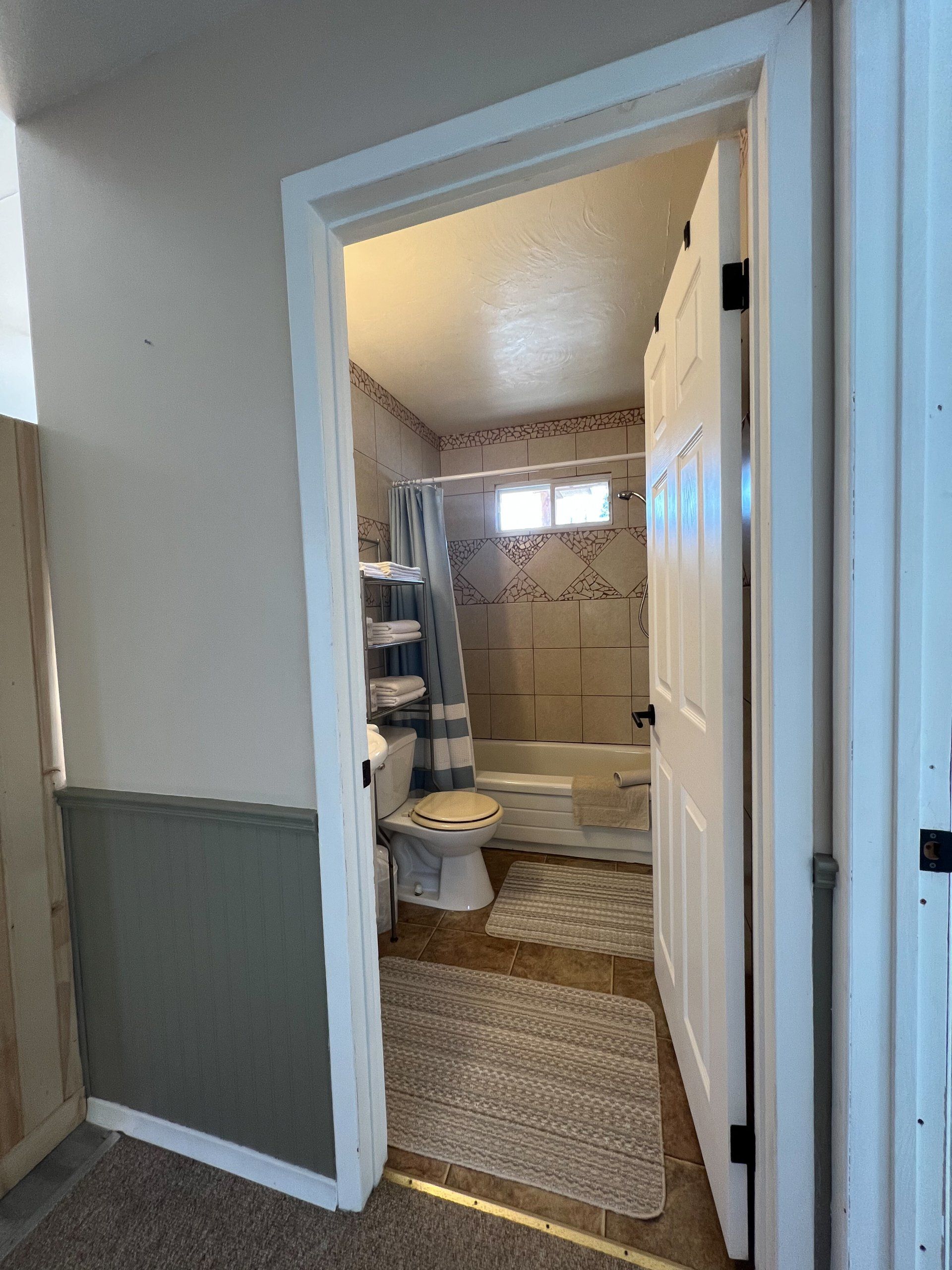 Doorway into a small bathroom with tiled shower, window, and white towels on a rack.