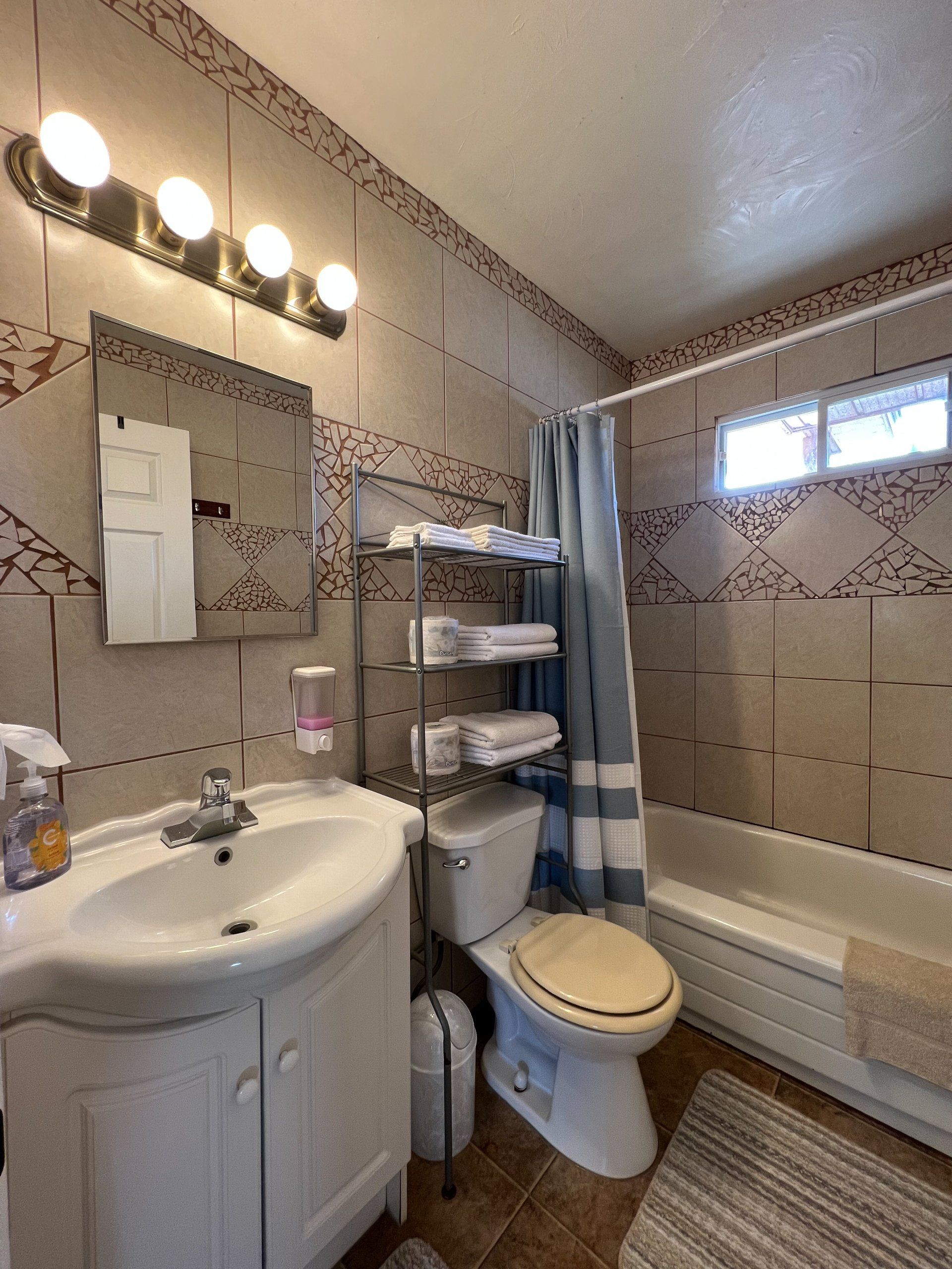 Small tiled bathroom with sink, toilet, bathtub, mirror, and window.