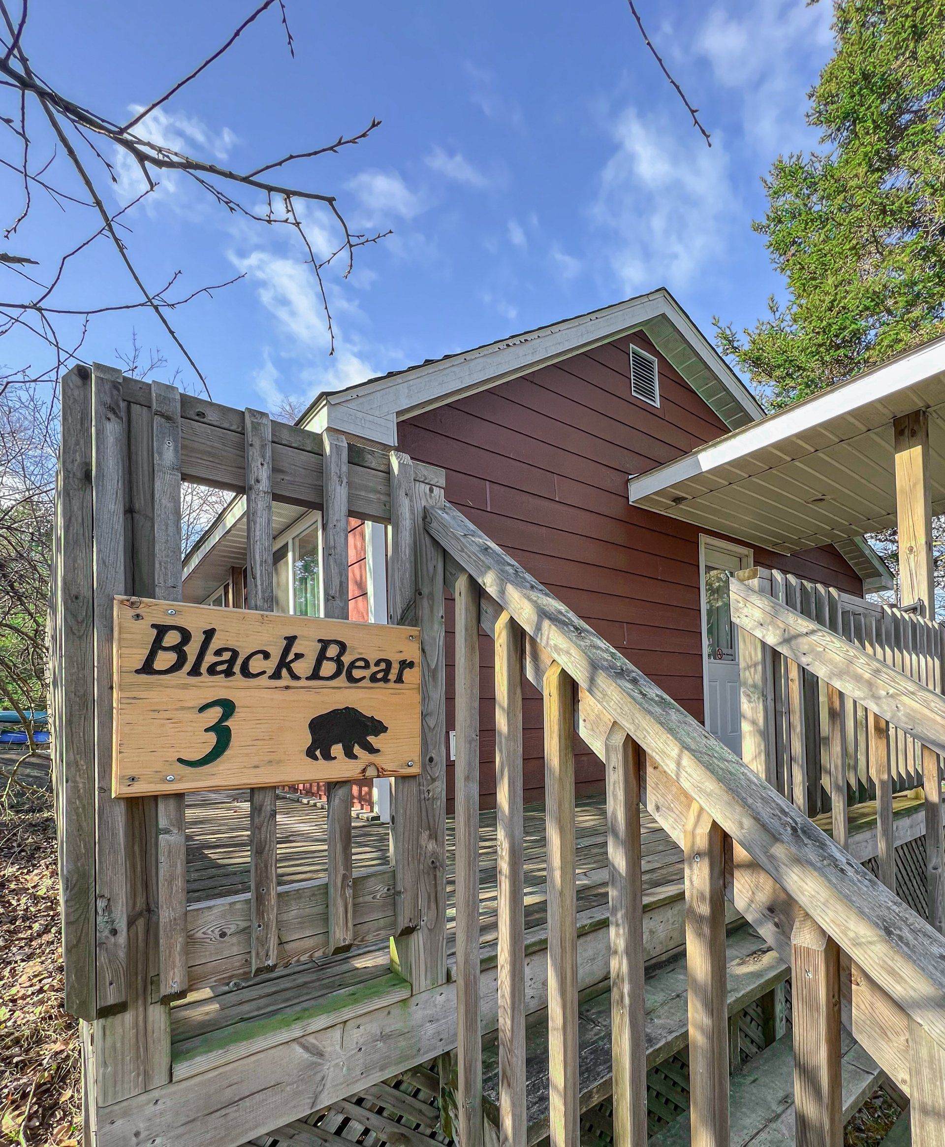 Wooden gate with “BlackBear 3” sign, beside rustic stairs and a house under a blue sky.