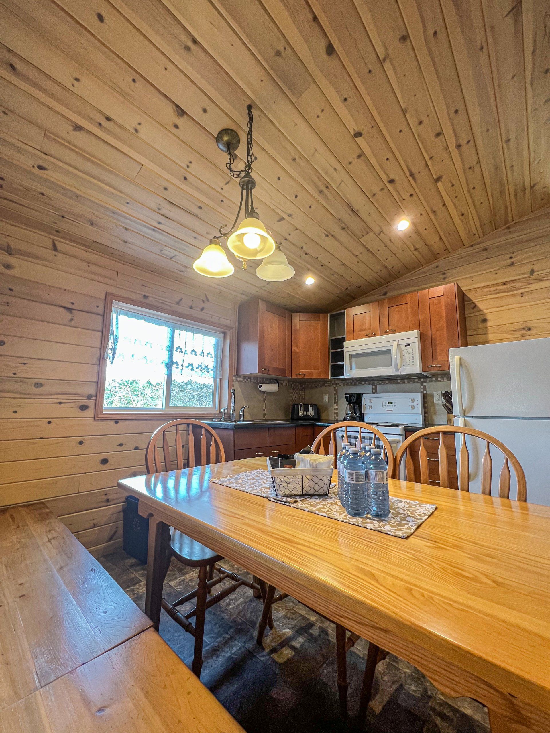 Wood-paneled cabin kitchen and dining area with wooden table, chairs, cabinets, and white refrigerator