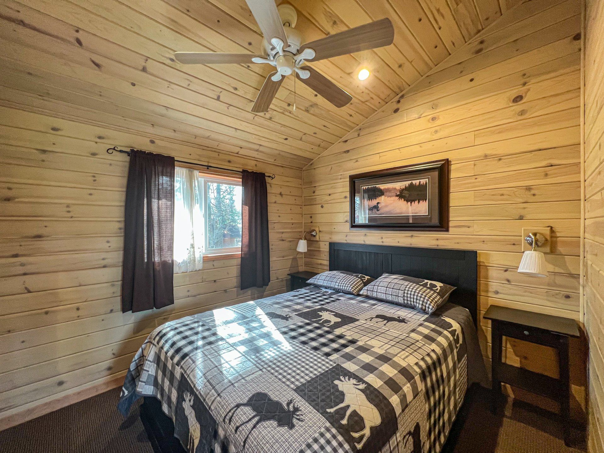 Rustic bedroom with log walls, a bed, window, ceiling fan, and framed landscape above the headboard