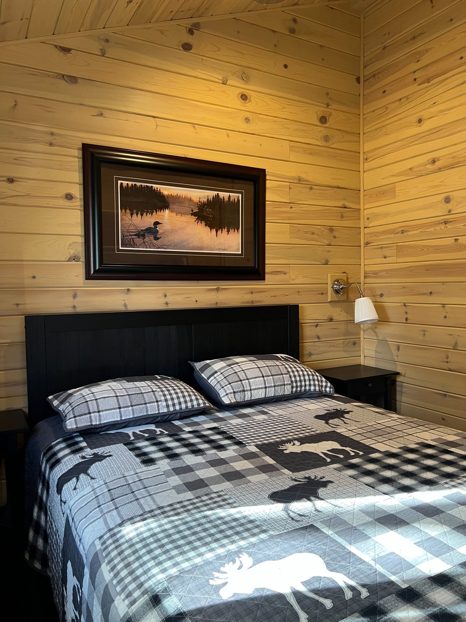 Cozy bedroom with black bed, patterned bedding, wood-paneled walls, and a framed landscape above the headboard