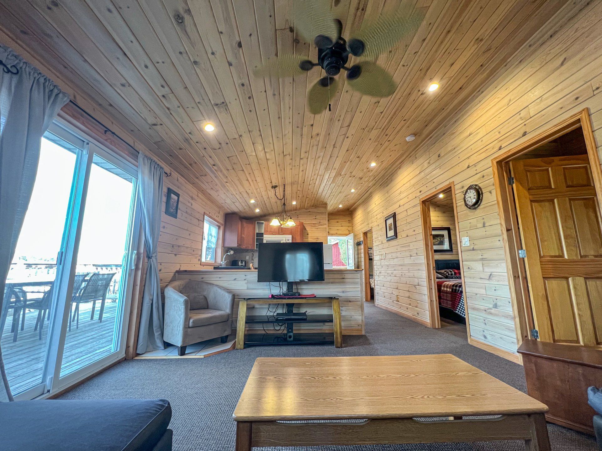 Cozy cabin living room with wood-paneled walls, TV, sofa, coffee table, and deck doors to the left