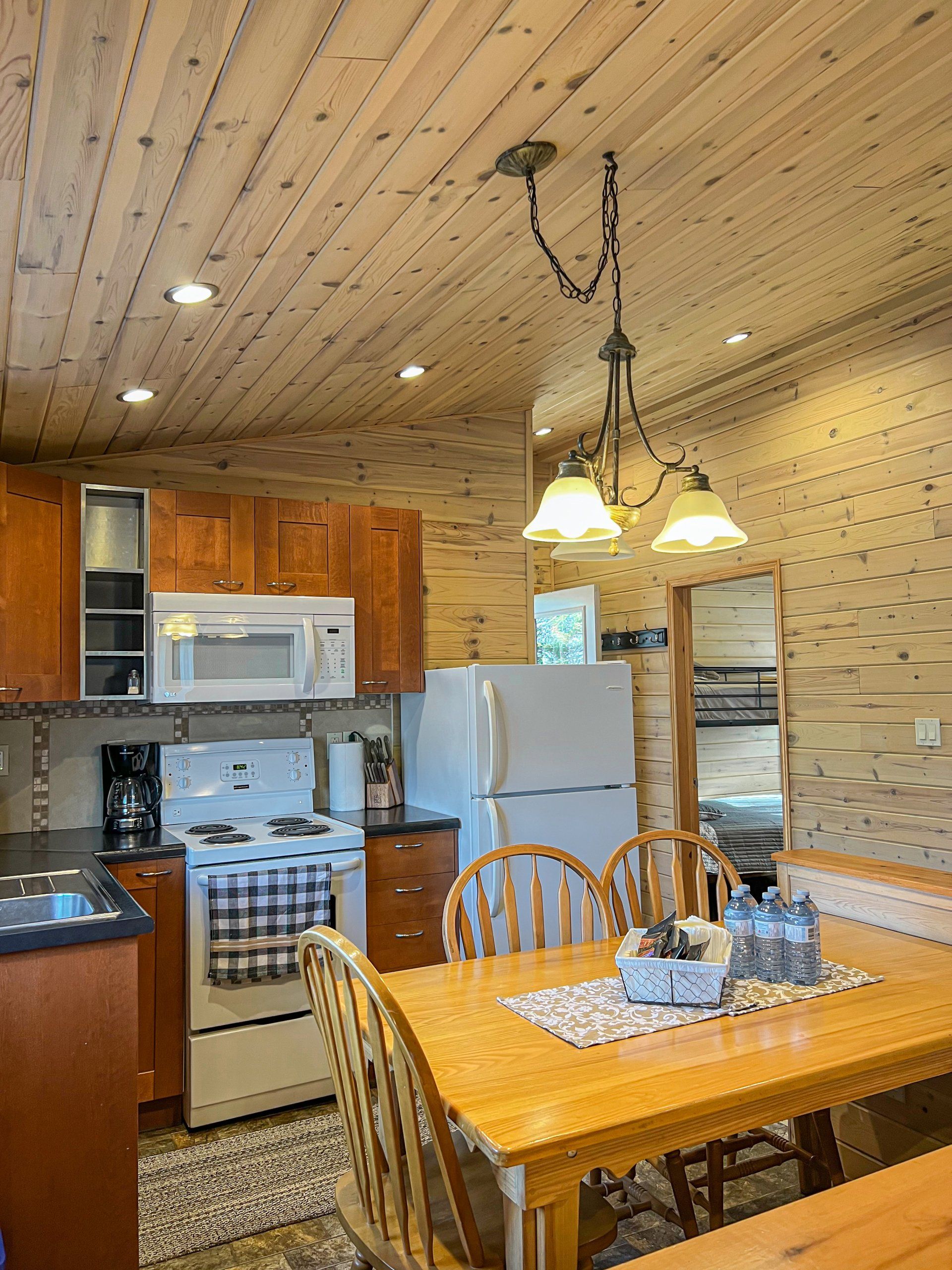 Cozy kitchen and dining area with wooden table, hanging lights, white appliances, and patterned wall decor