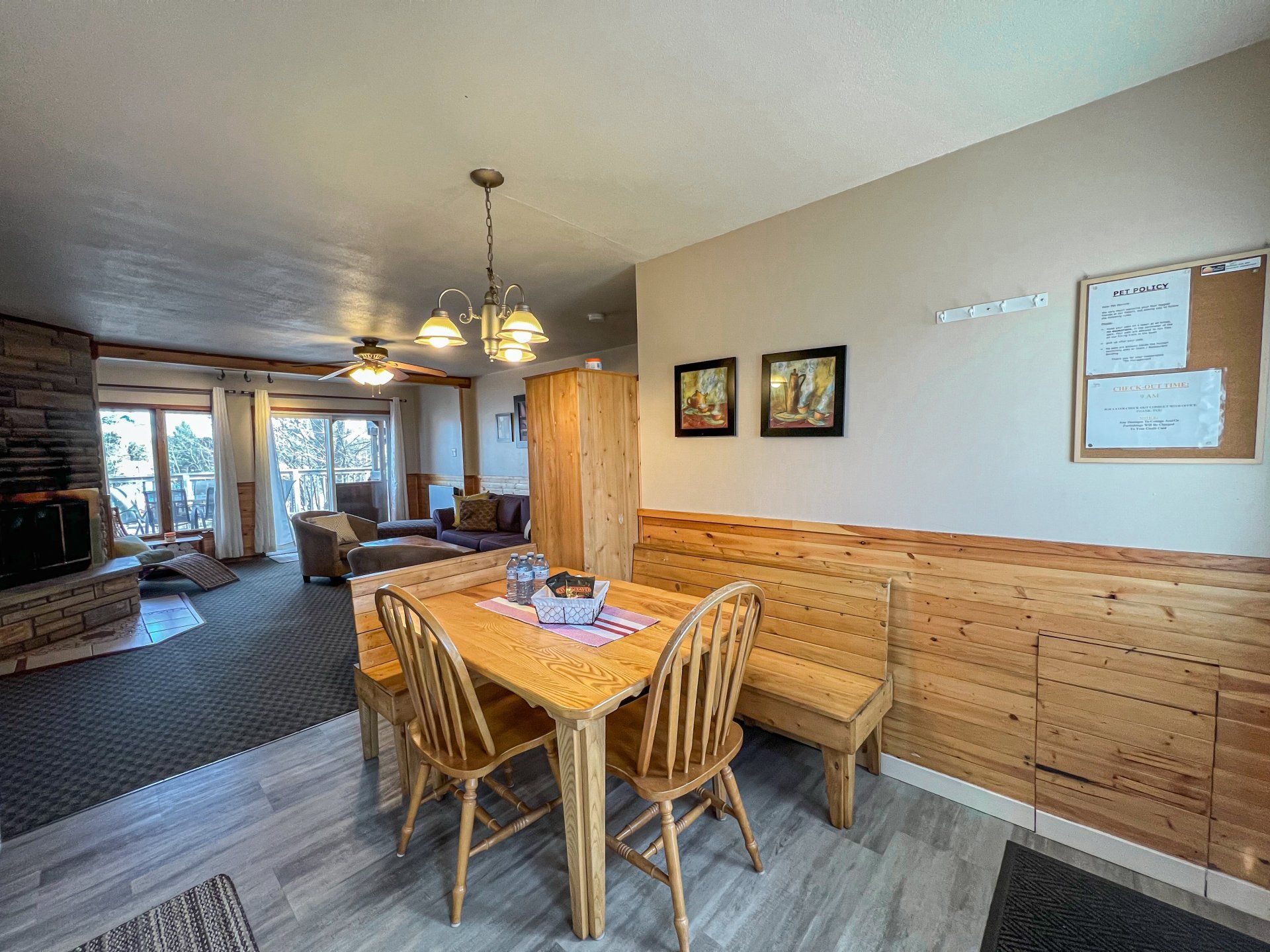Dining area with wicker table, wood-paneled walls, and a cozy living room beyond.
