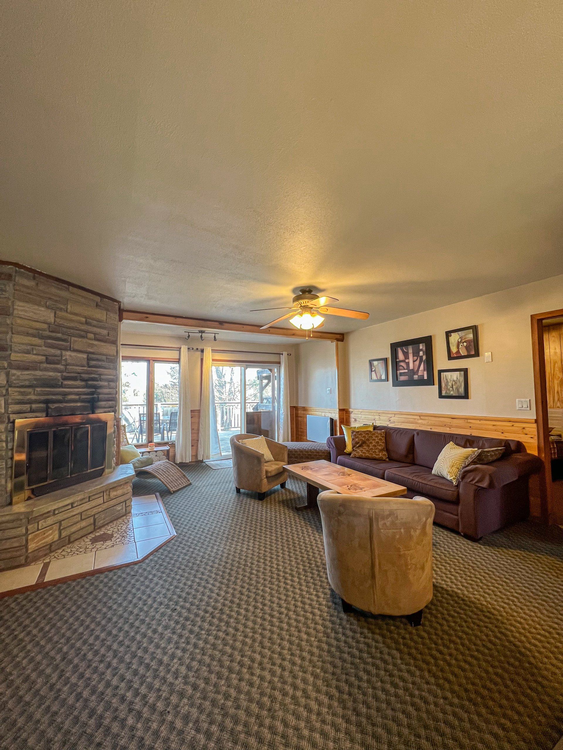Spacious living room with stone fireplace, brown sofa, patterned carpet, and sliding doors to a bright sunroom.