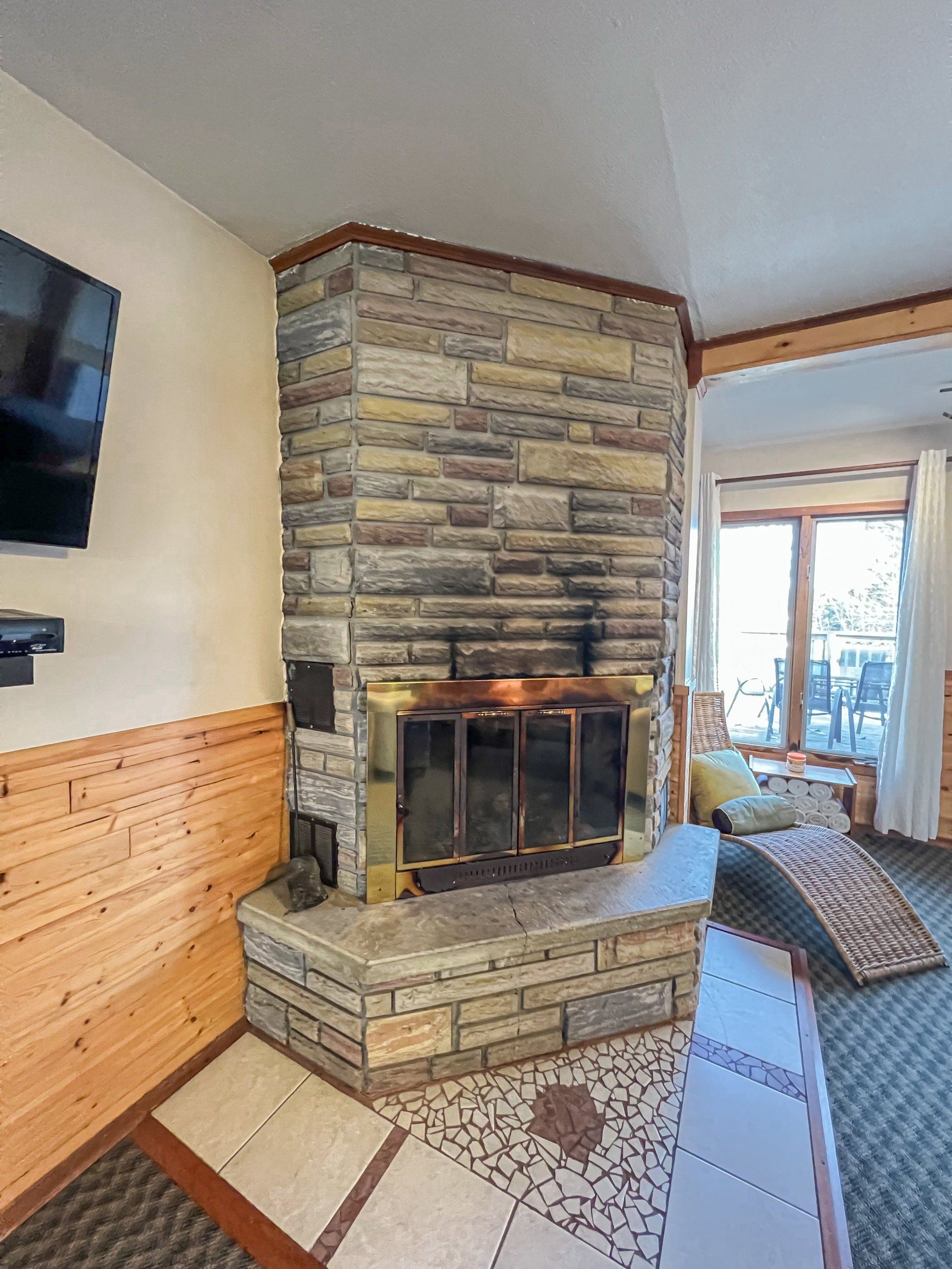 Stone fireplace in a living room with a TV on the wall and tiled floor.