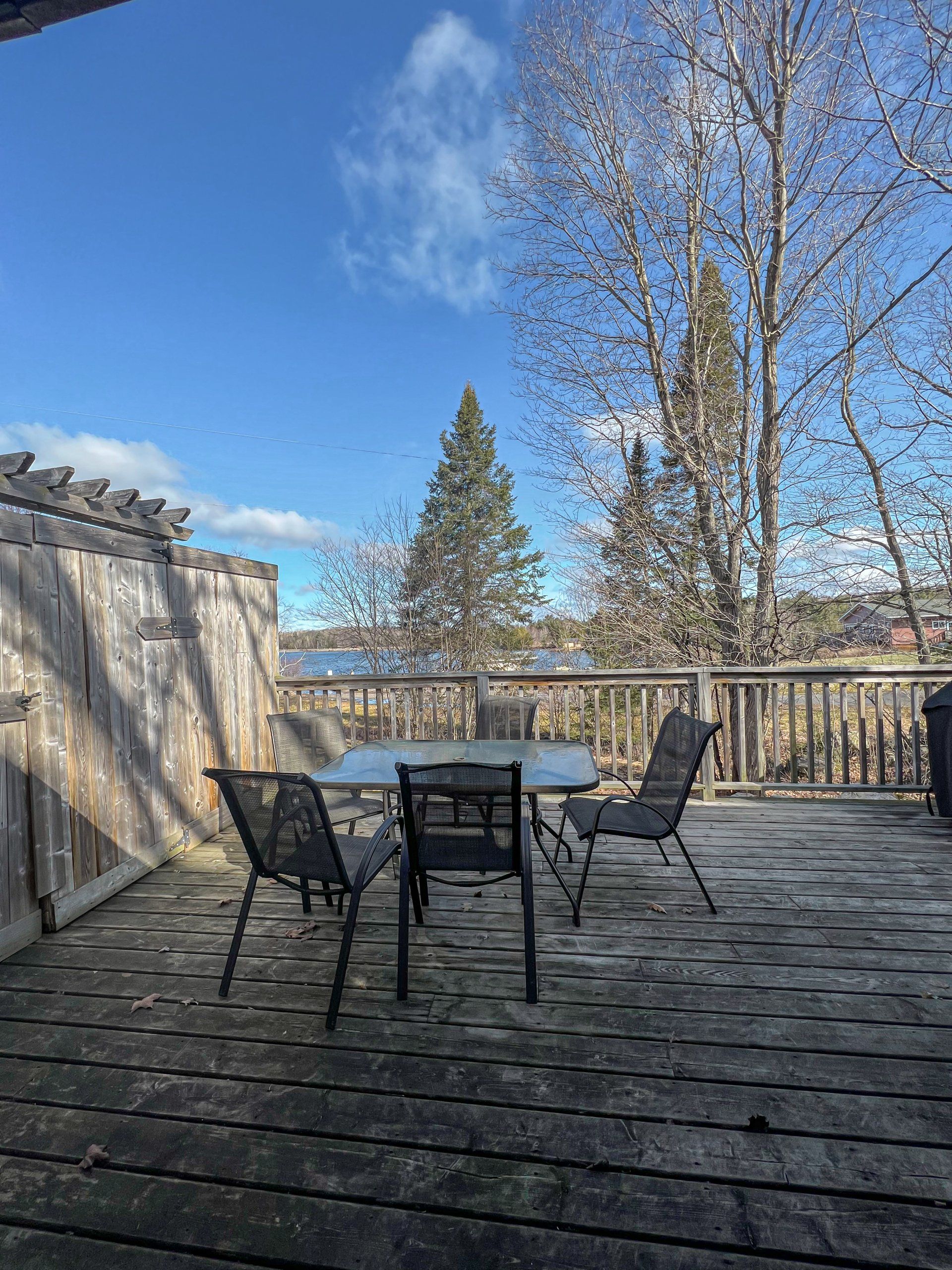 Patio with black chairs and table overlooking a lake under a blue sky with bare trees