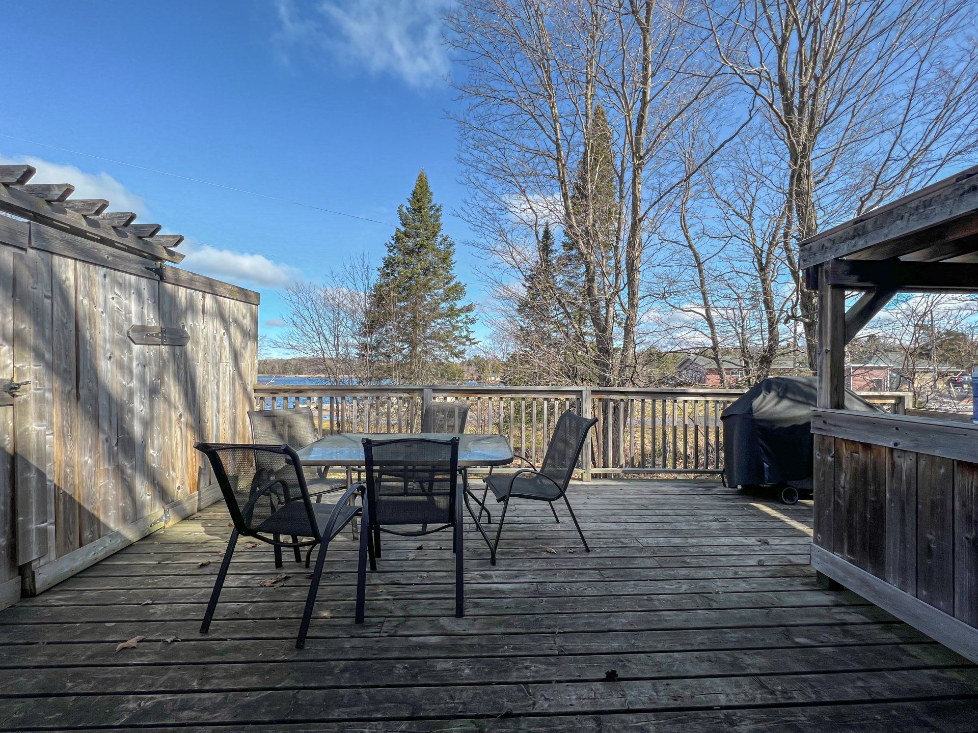 Wooden deck with patio table and chairs, overlooking bare trees under a clear blue sky.