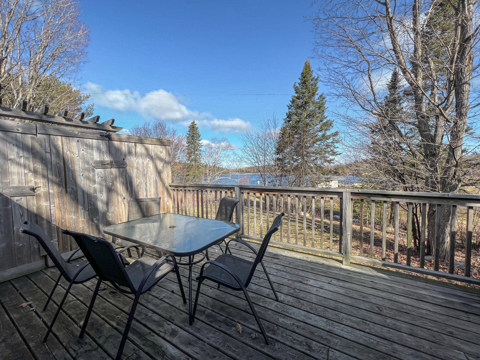 Wooden deck with black chairs and glass table, overlooking trees and a blue sky