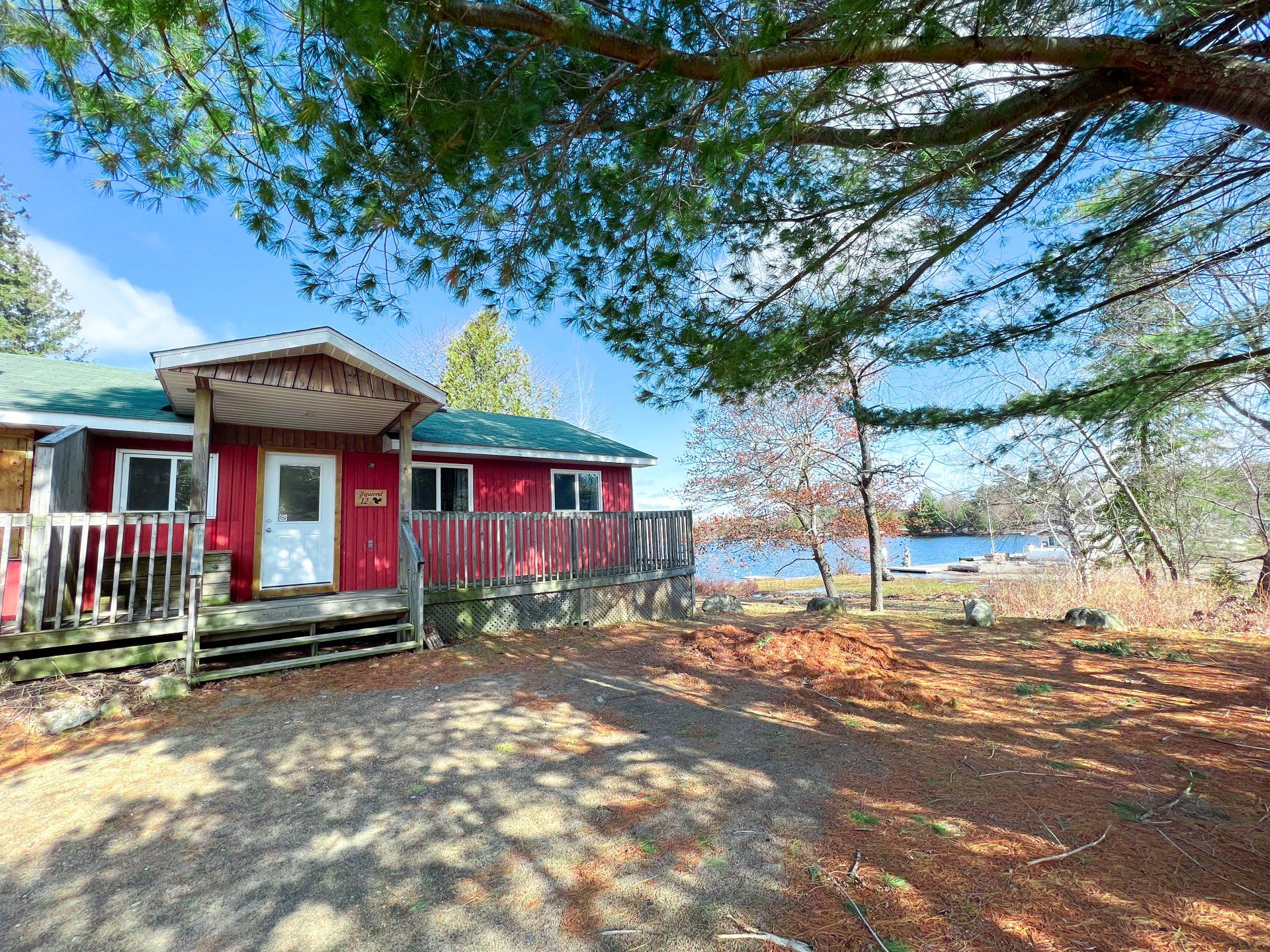 Red cabin with porch by a lakeside, framed by tree branches and autumn leaves