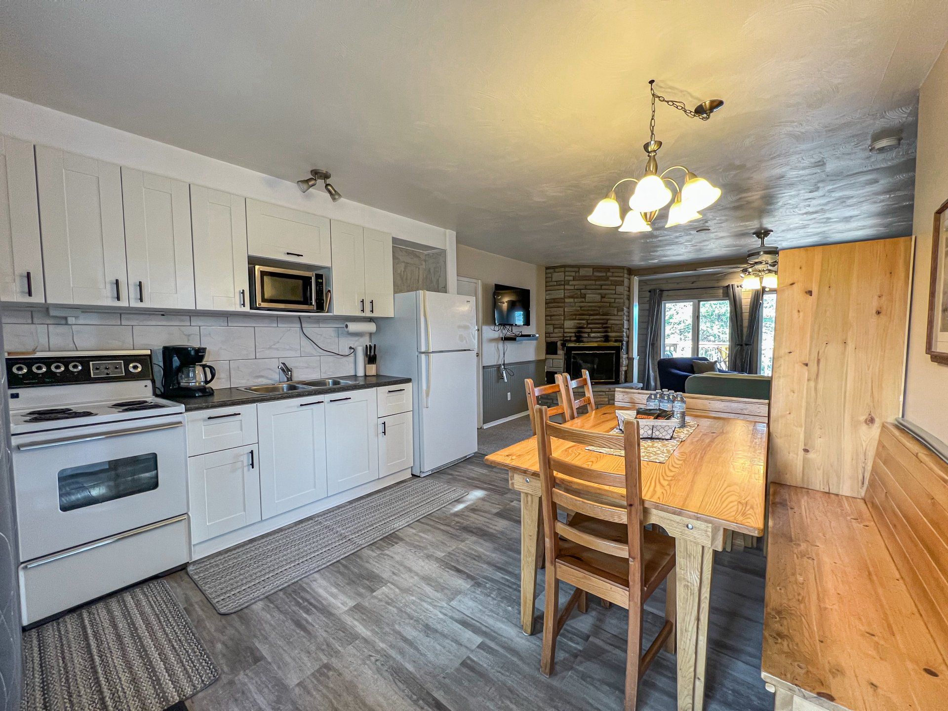 Bright kitchen and dining area with white cabinets, stainless fridge, wooden table, and chandelier