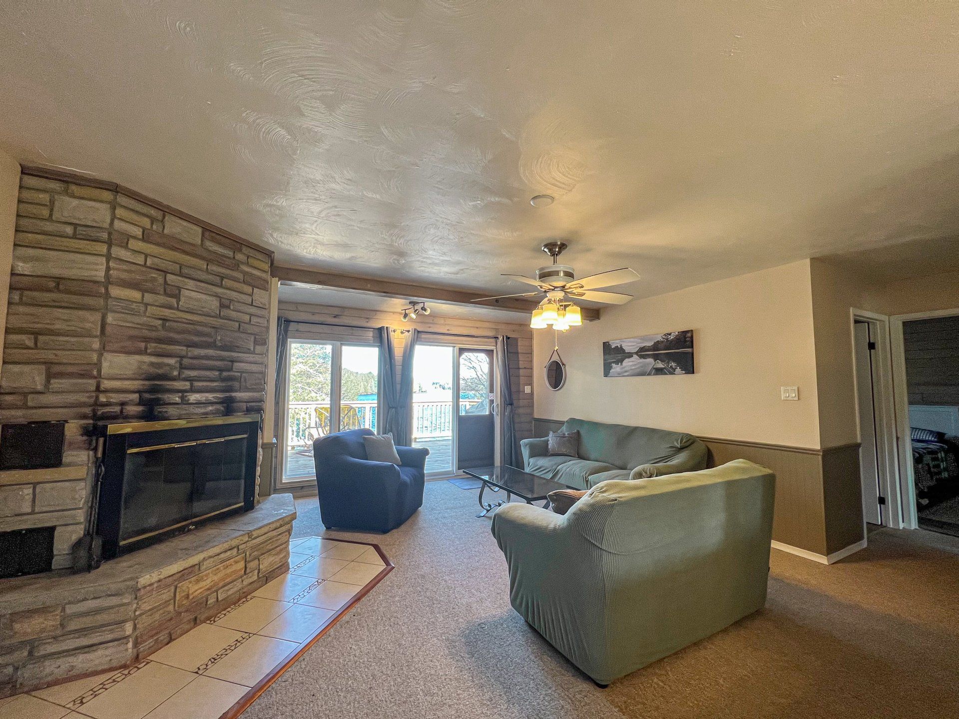 Living room with stone fireplace, green sofa, blue chair, and sliding glass doors to a patio