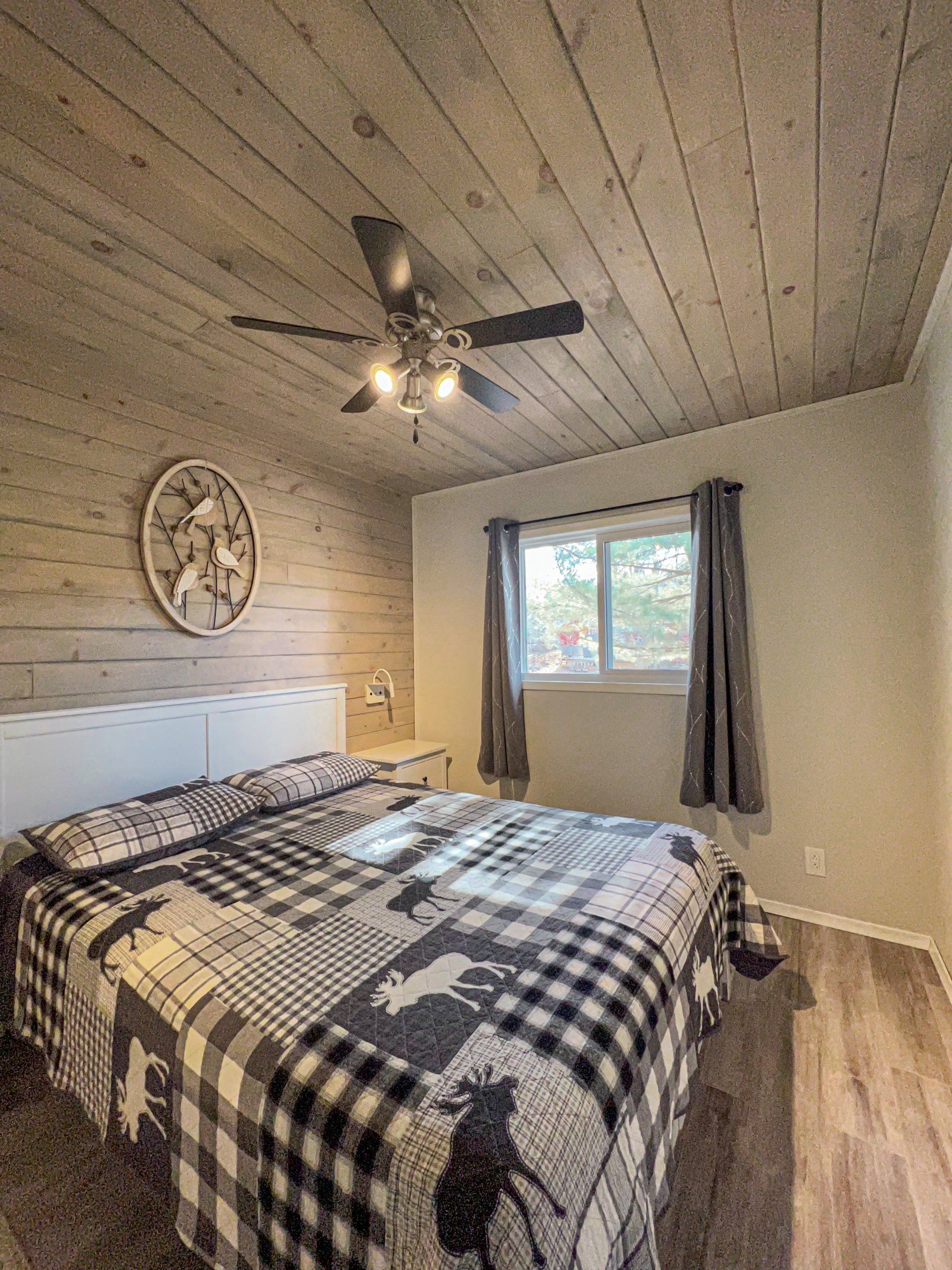 Cozy bedroom with plaid bedspread, ceiling fan, wall art, and window with curtains