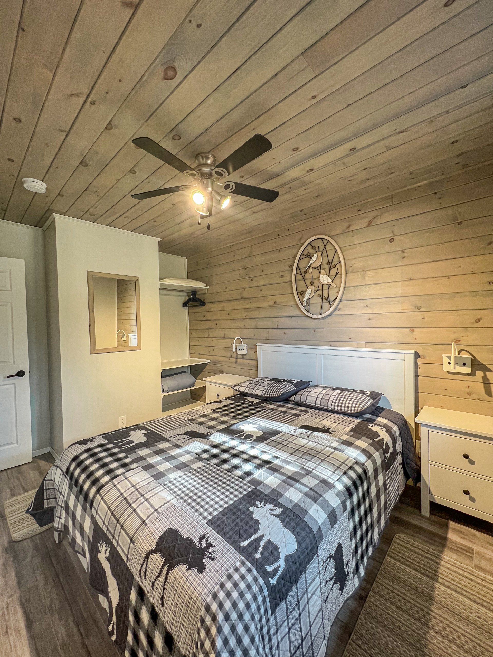 Cozy bedroom with a bed, white dresser, wood-paneled walls and ceiling, and a ceiling fan