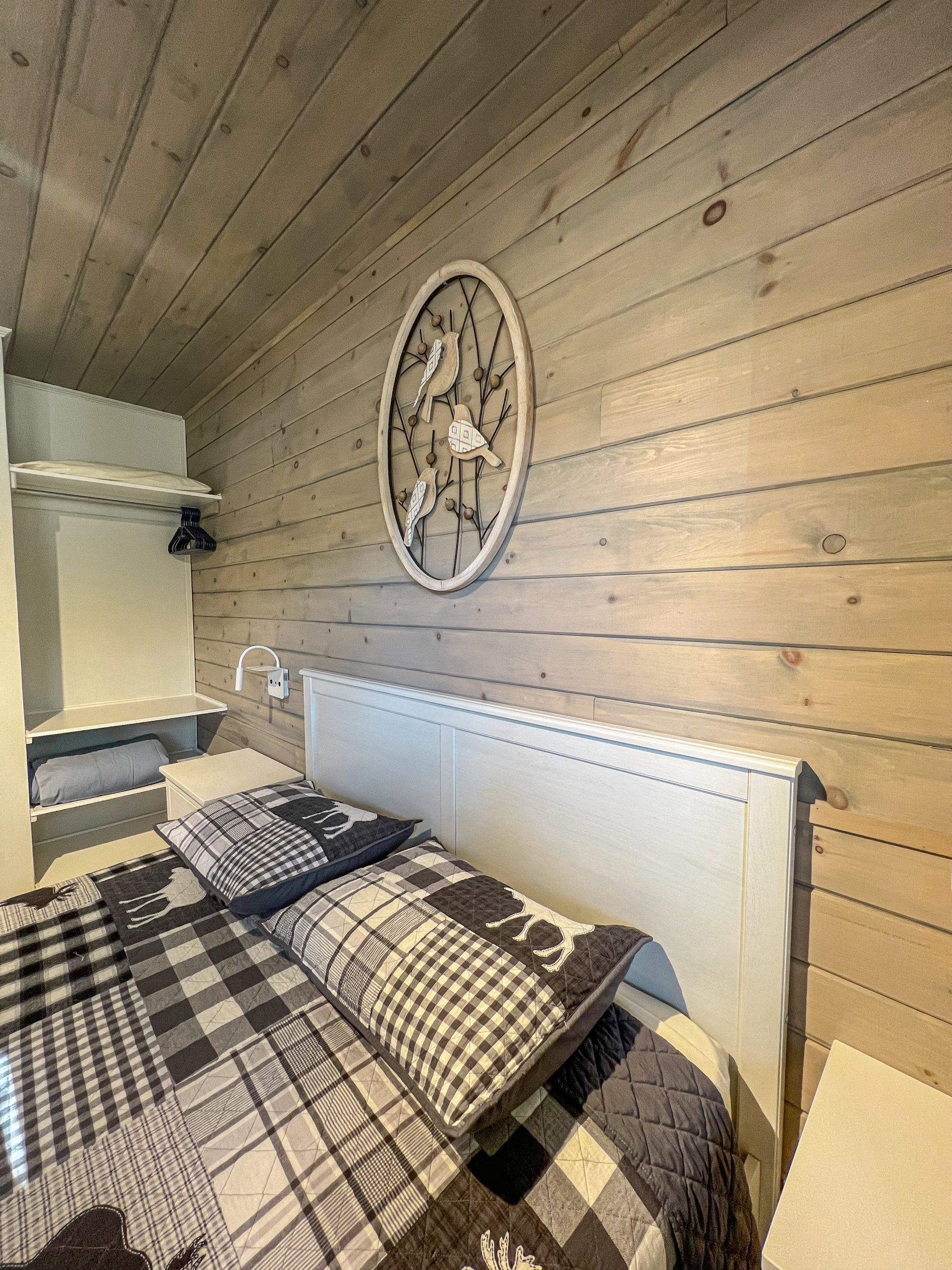 Cozy bedroom with plaid bedding, wood-paneled walls, and a round wall clock above the bed