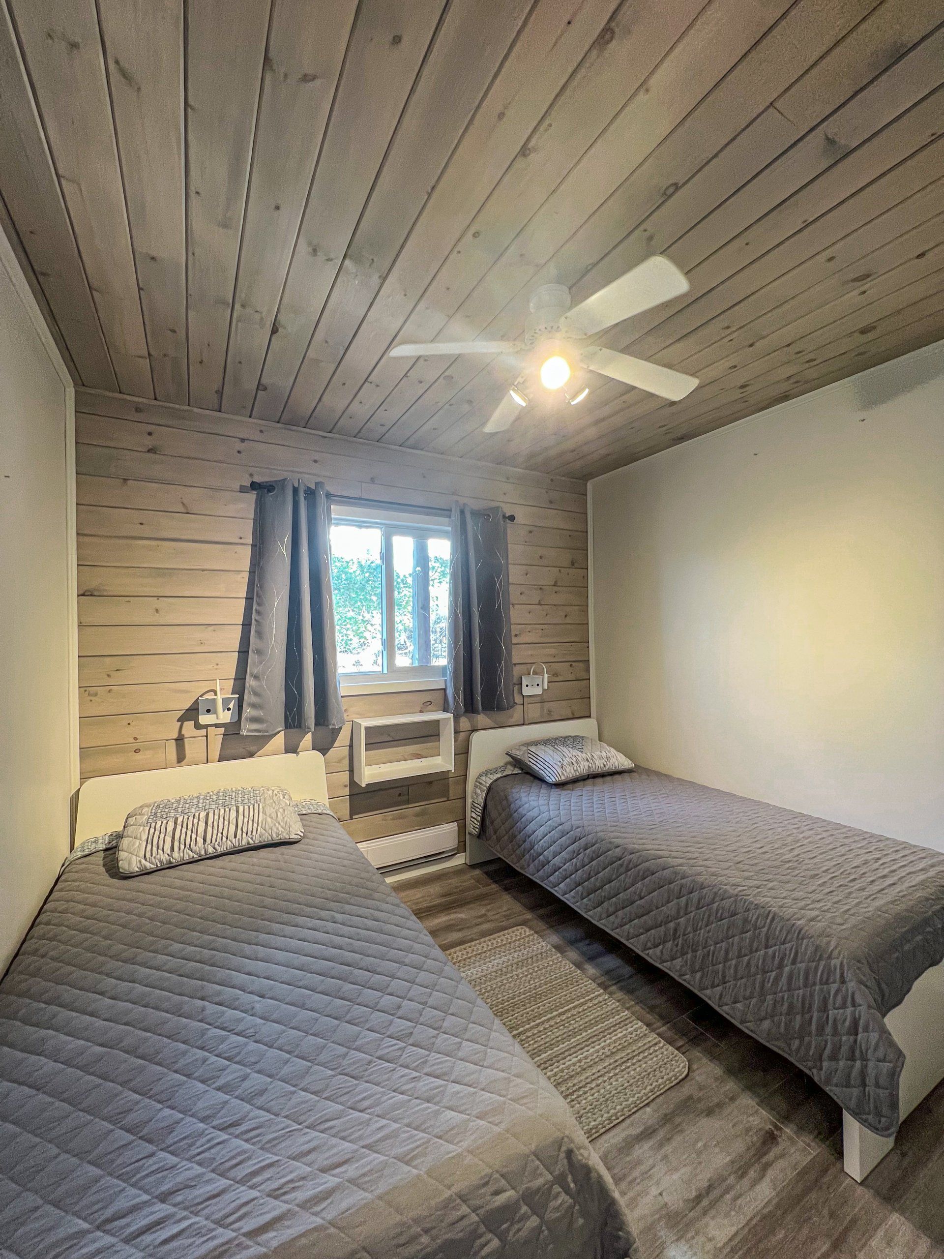 Small bedroom with two single beds, wood-paneled ceiling, window, and ceiling fan.