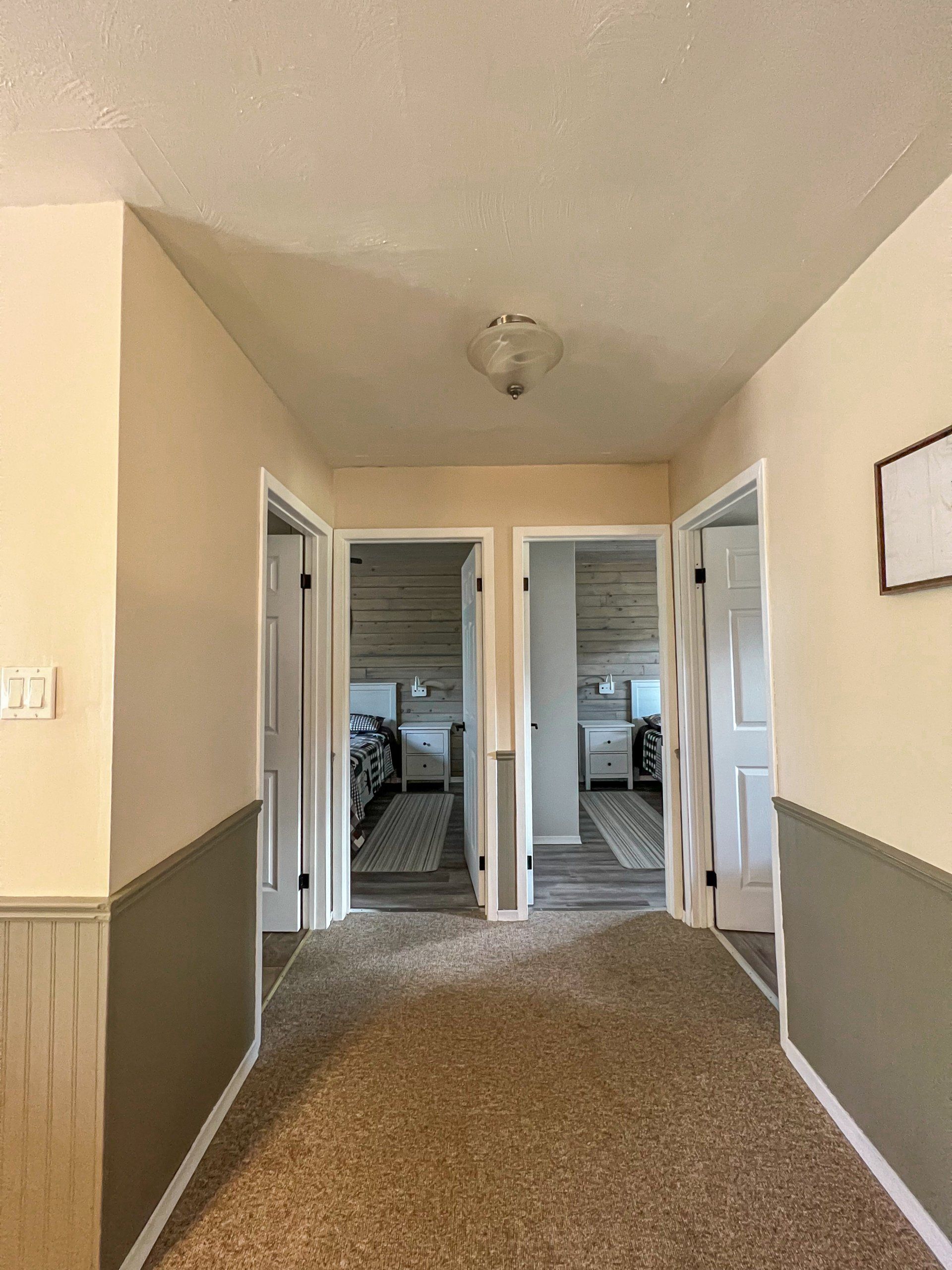Narrow carpeted hallway with open white doors and a stairway visible at the far end.