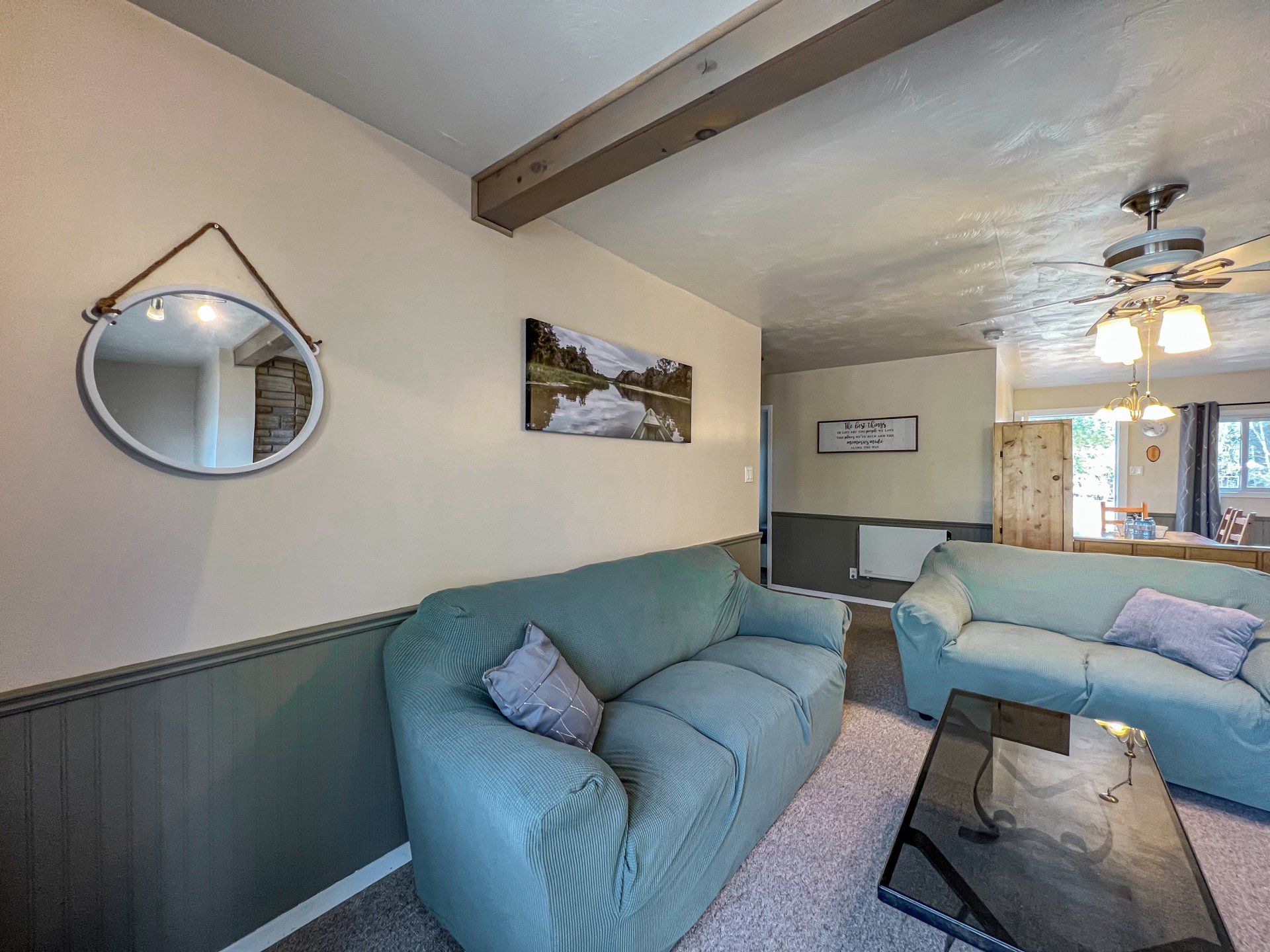 Cozy living room with blue sofas, mirror wall decor, and a glass coffee table under a ceiling fan.