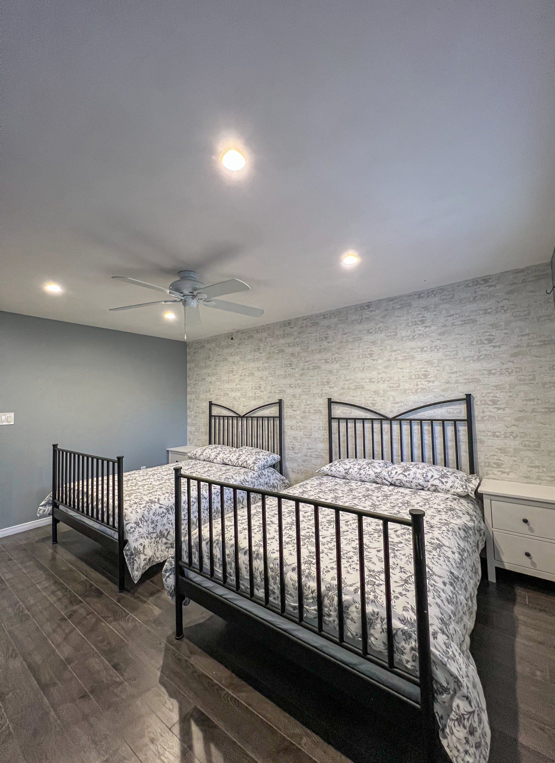 Bedroom with three black metal beds, gray walls, ceiling fan, and wood flooring
