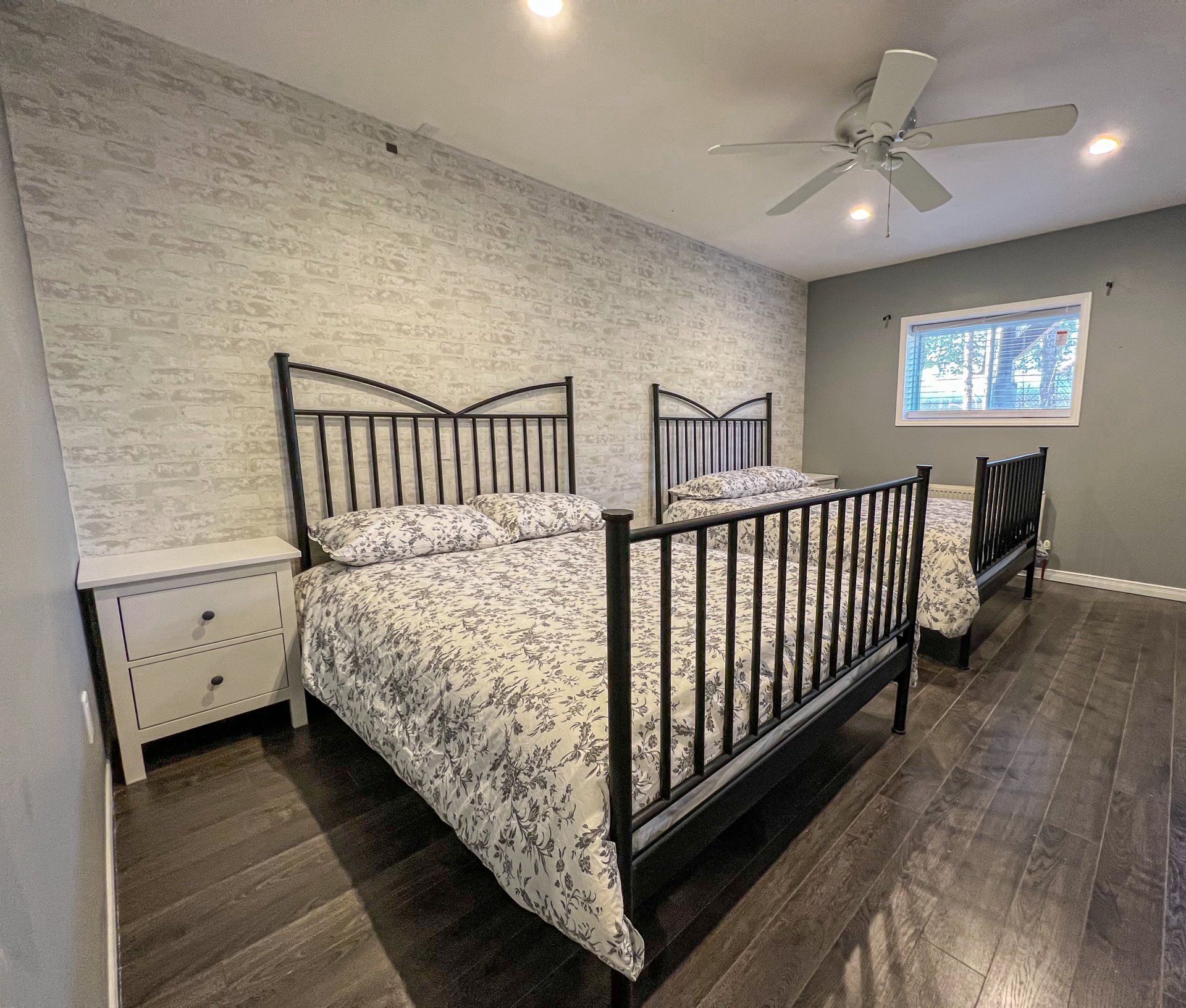 Bedroom with black metal bed frame, patterned bedding, nightstand, ceiling fan, and window