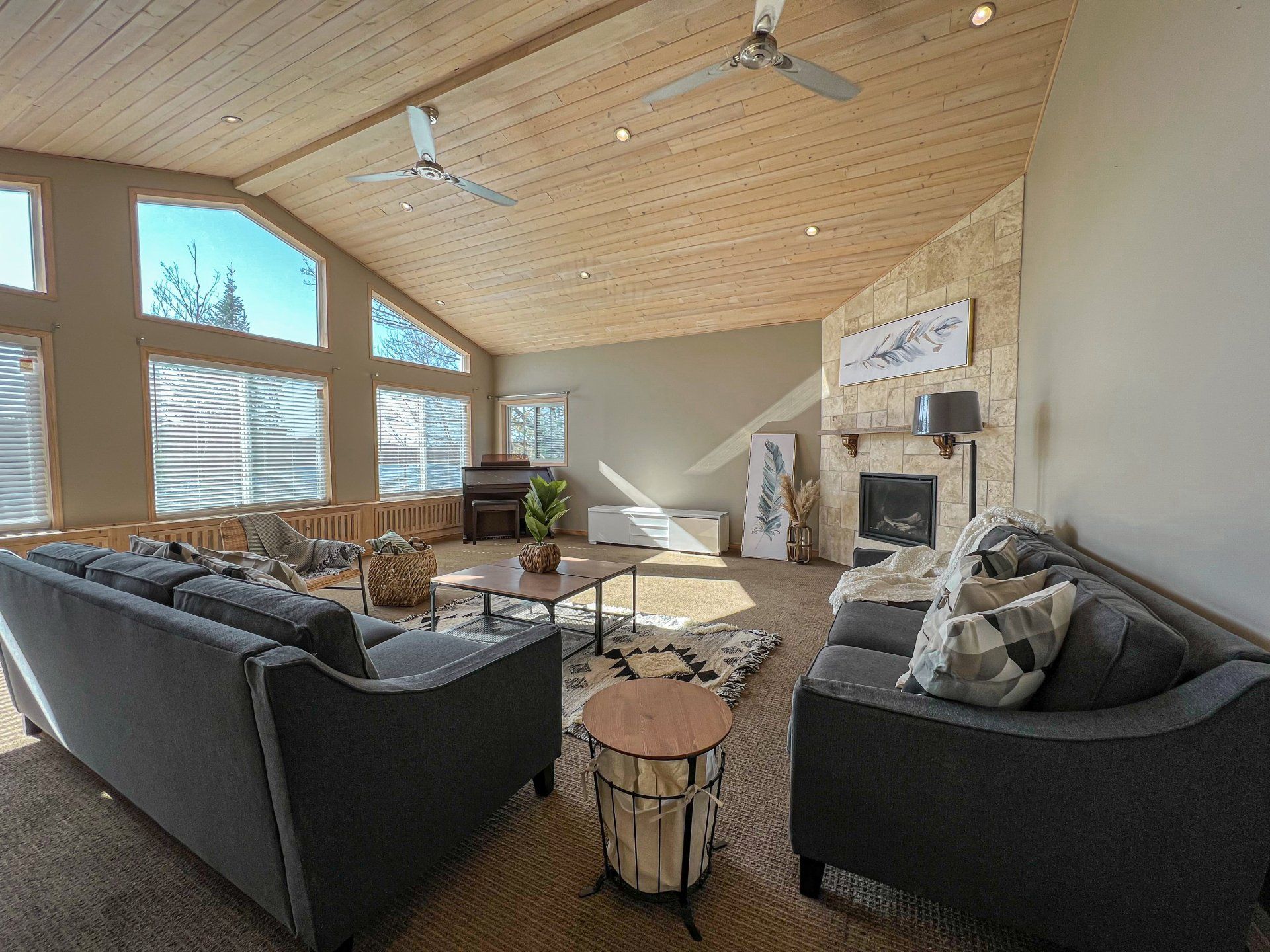 Modern living room with gray sofas, large windows, wood ceiling, and a stone fireplace