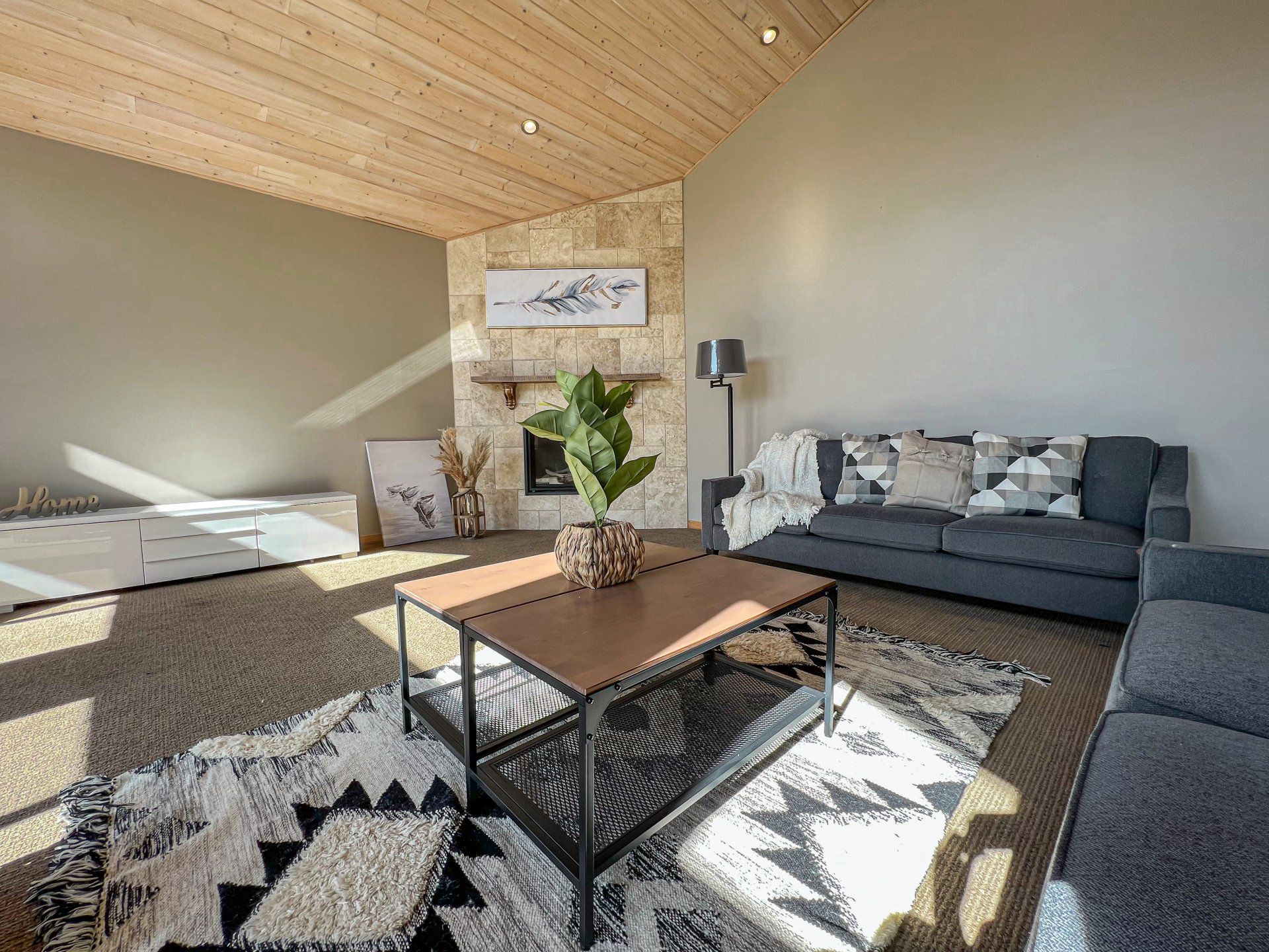 Bright living room with gray sofa, patterned rug, coffee table, and sunlight on a wooden ceiling