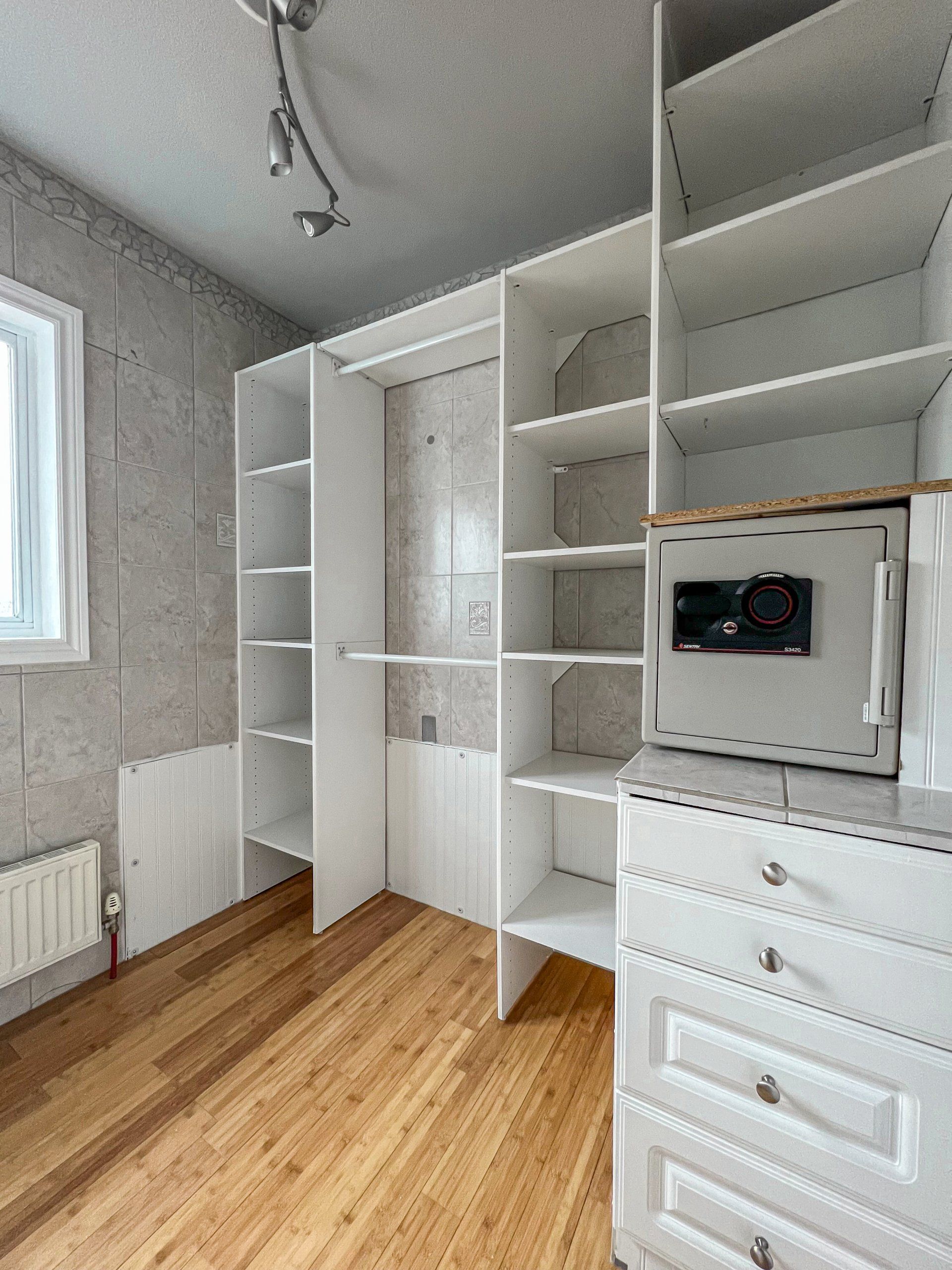 White built-in wardrobe and shelving in a bright room with wood floor and a small window.