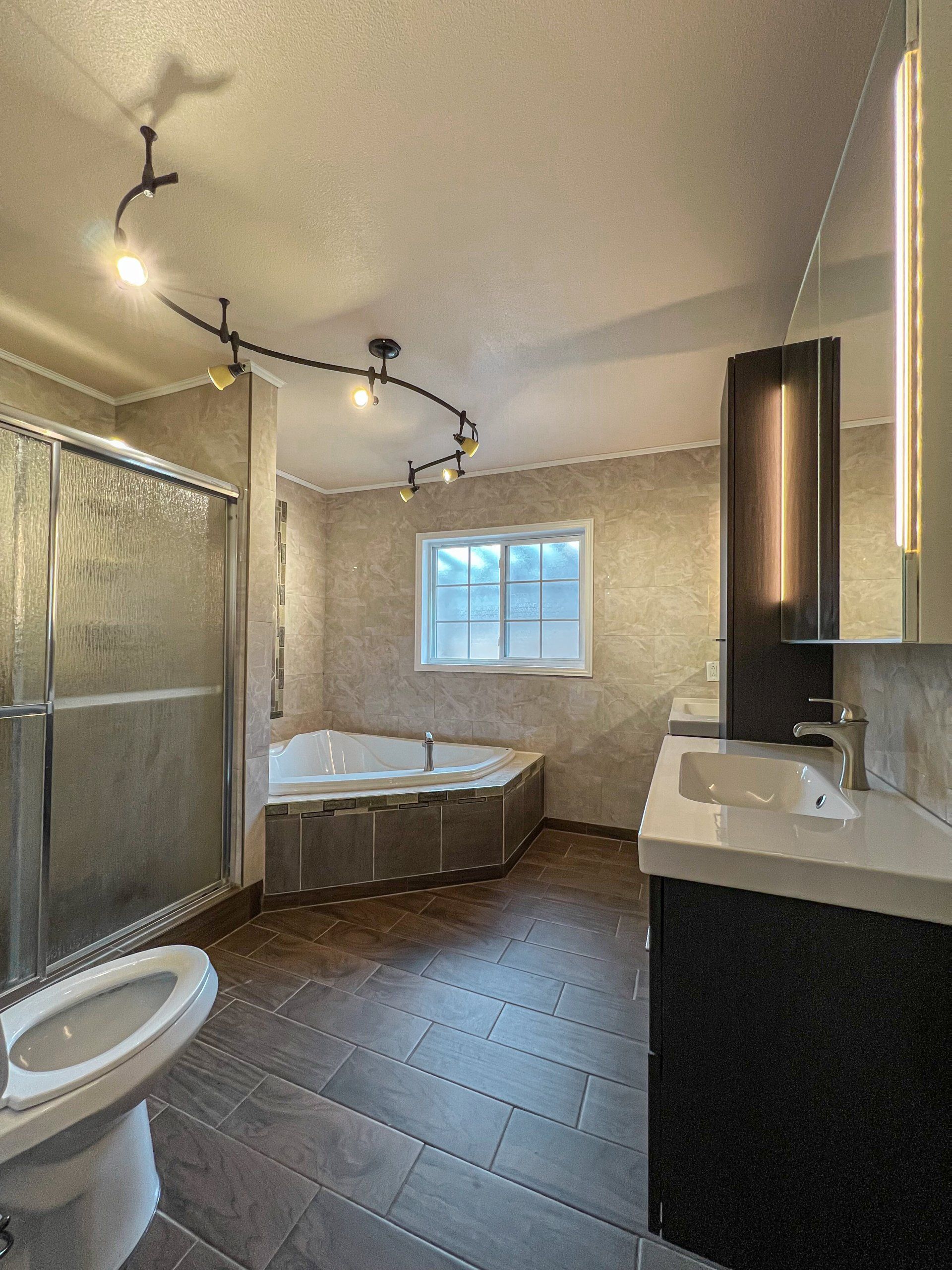 Small bathroom with a corner bathtub, glass shower, sink vanity, toilet, and dark tile floor.