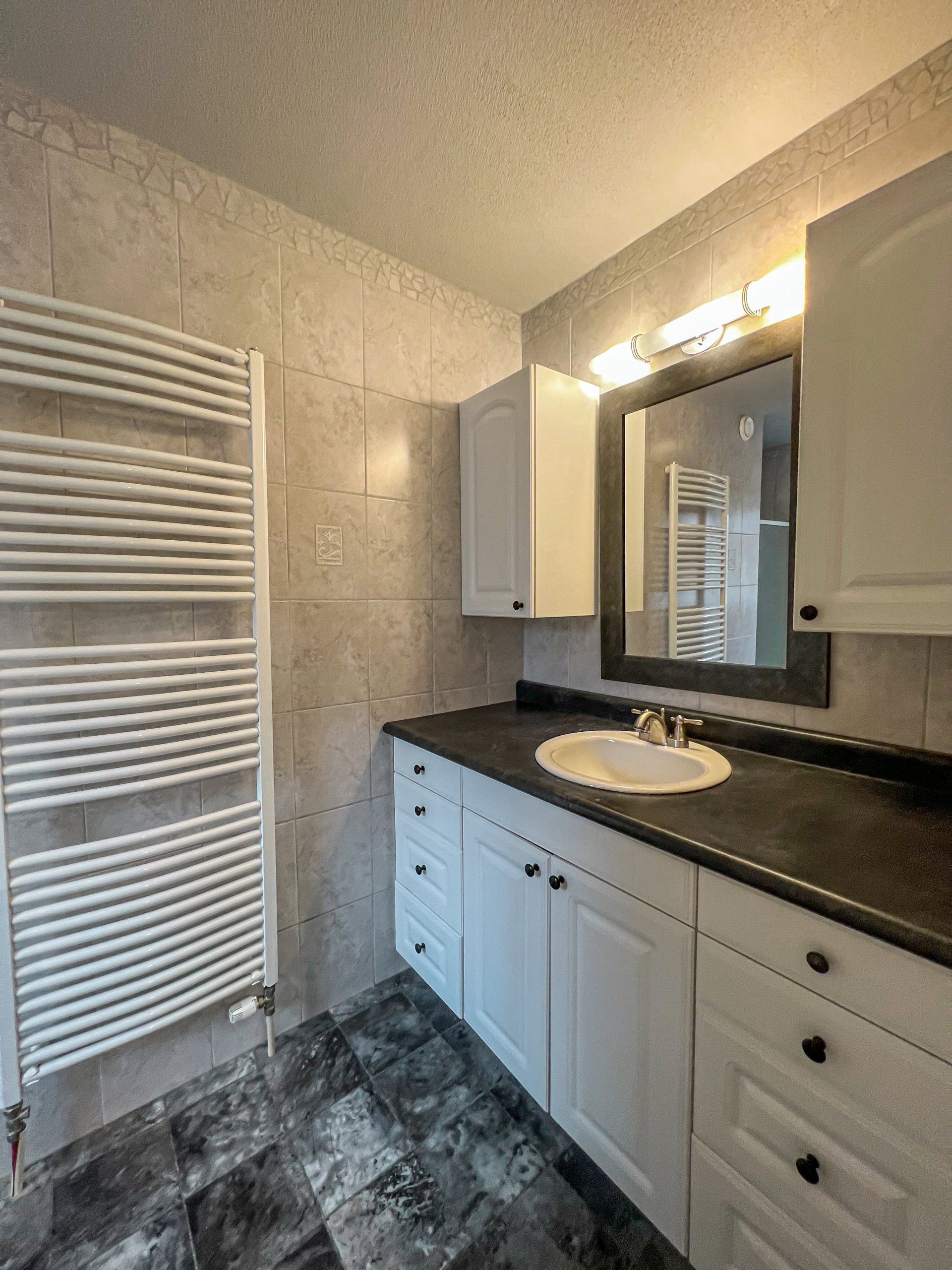 Modern bathroom with white vanity, black countertop, mirror lights, and white towel radiator.
