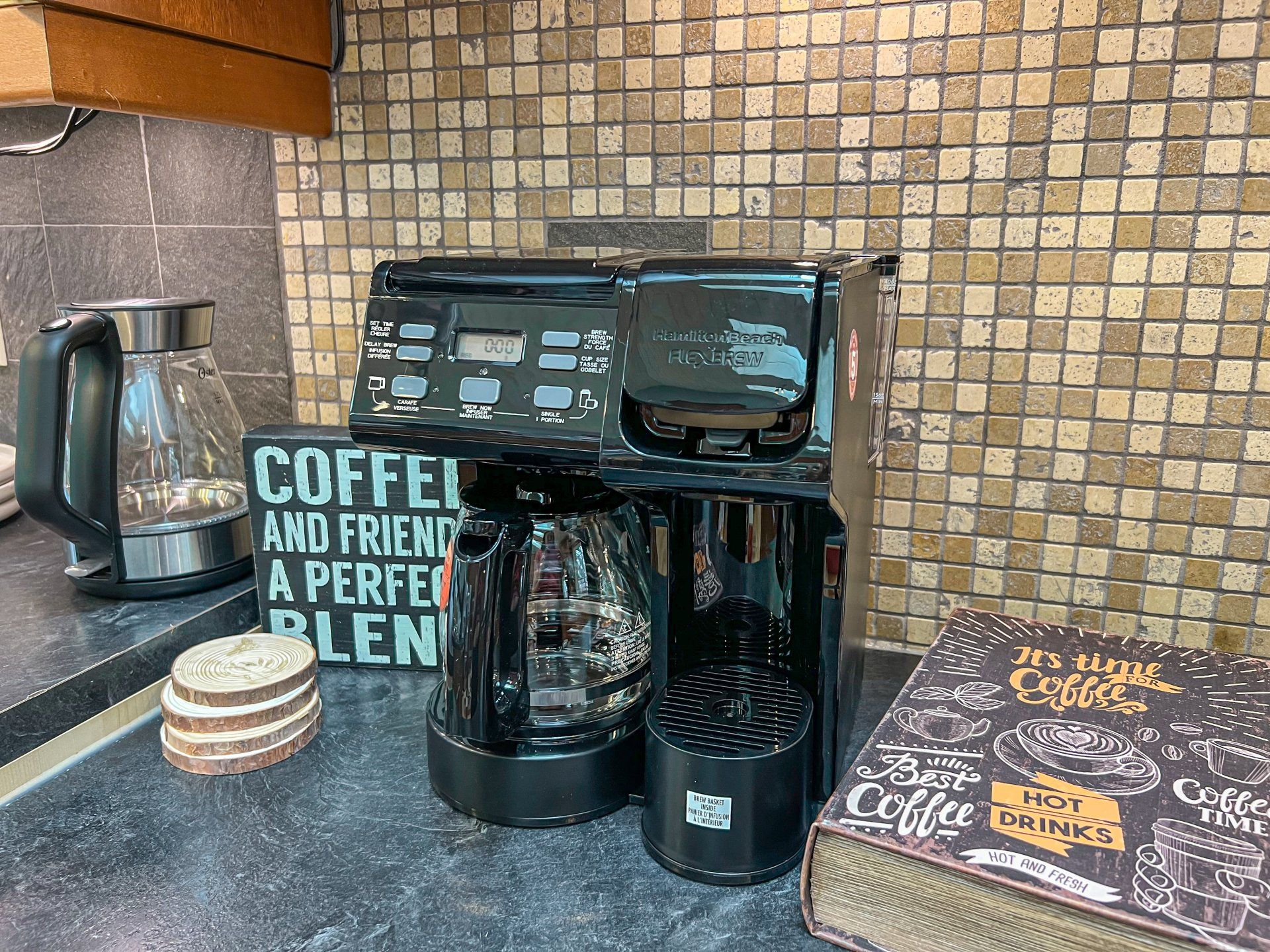 Black coffee maker and kettle on a kitchen counter beside a sign reading “Coffee and friends are a perfect blend.”