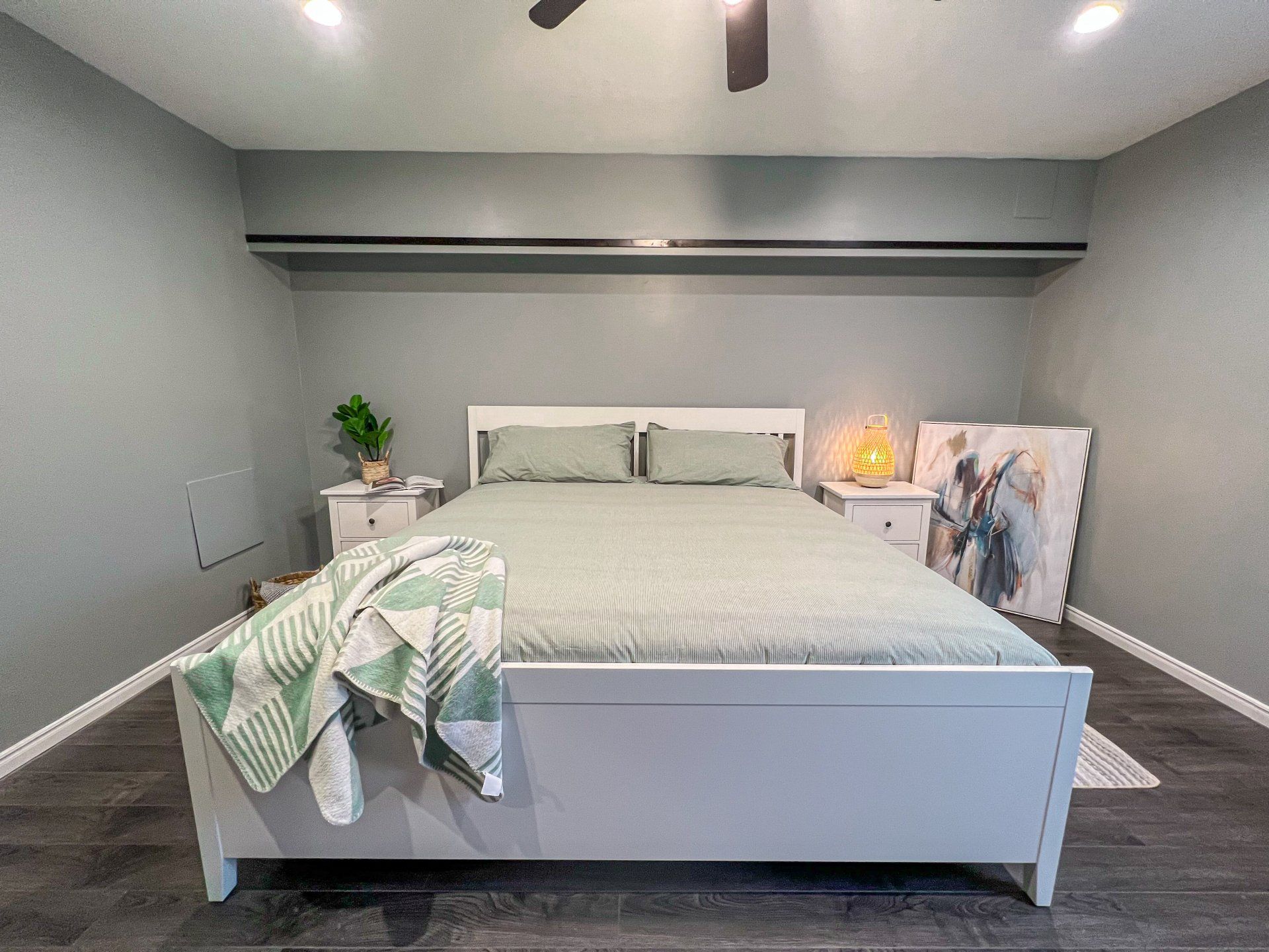 Neat gray bedroom with a bed, green throw blanket, and soft lamp lighting