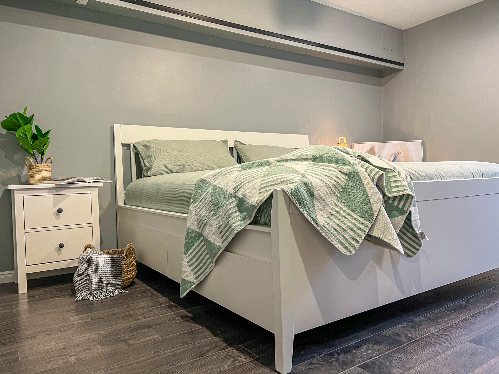 Cozy bedroom with a white bed, green bedding, bedside table, and a cat-shaped ottoman on dark wood floors