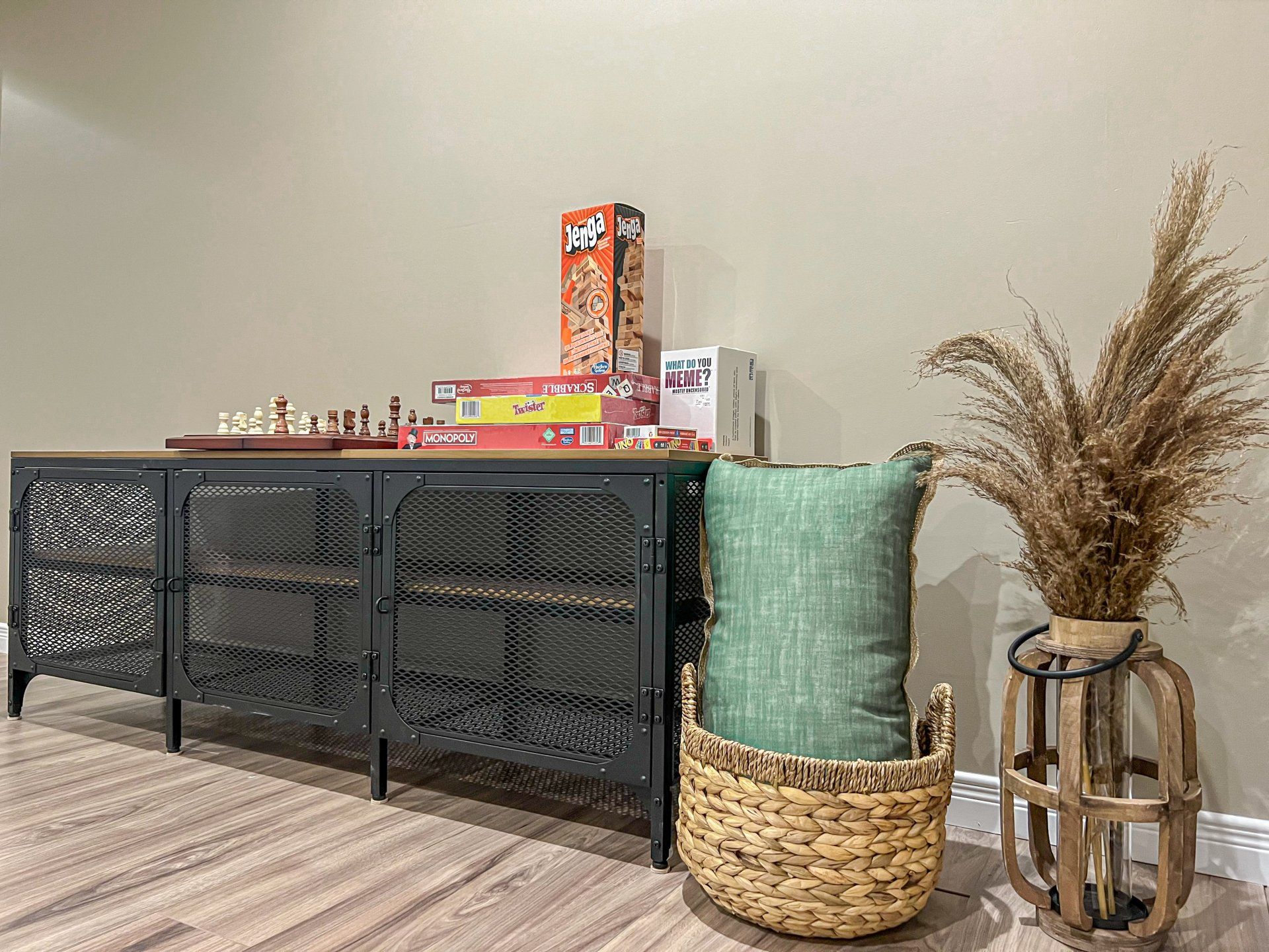 Black metal console table with board games, woven baskets, and dried pampas grass against a beige wall