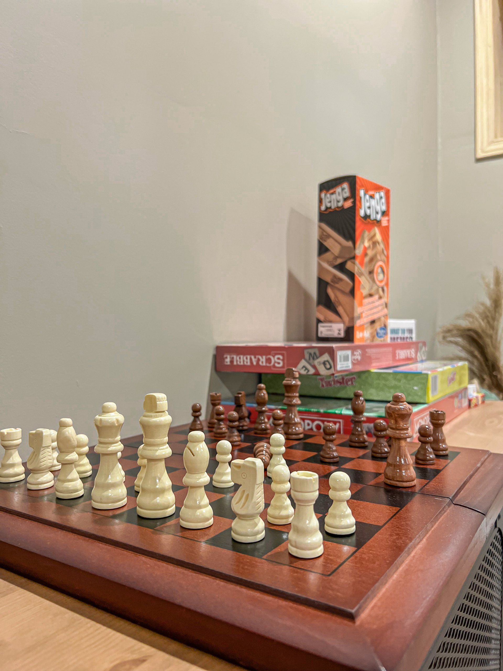 Chessboard with a set-up game in progress, white and brown pieces on a wooden table, with board game boxes behind.