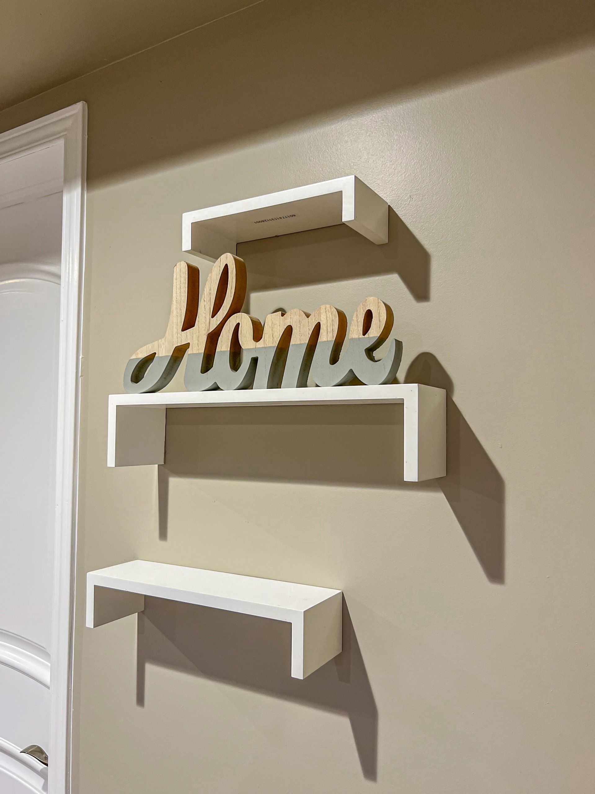 Wall shelves around a wooden “home” sign on a beige wall by a window